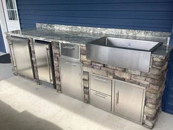 Outdoor kitchen with stainless steel appliances, stone facade, granite countertop, and stainless steel sink.