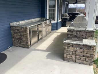 Outdoor kitchen with stone veneer, granite countertops, and stainless steel appliances on a covered patio.