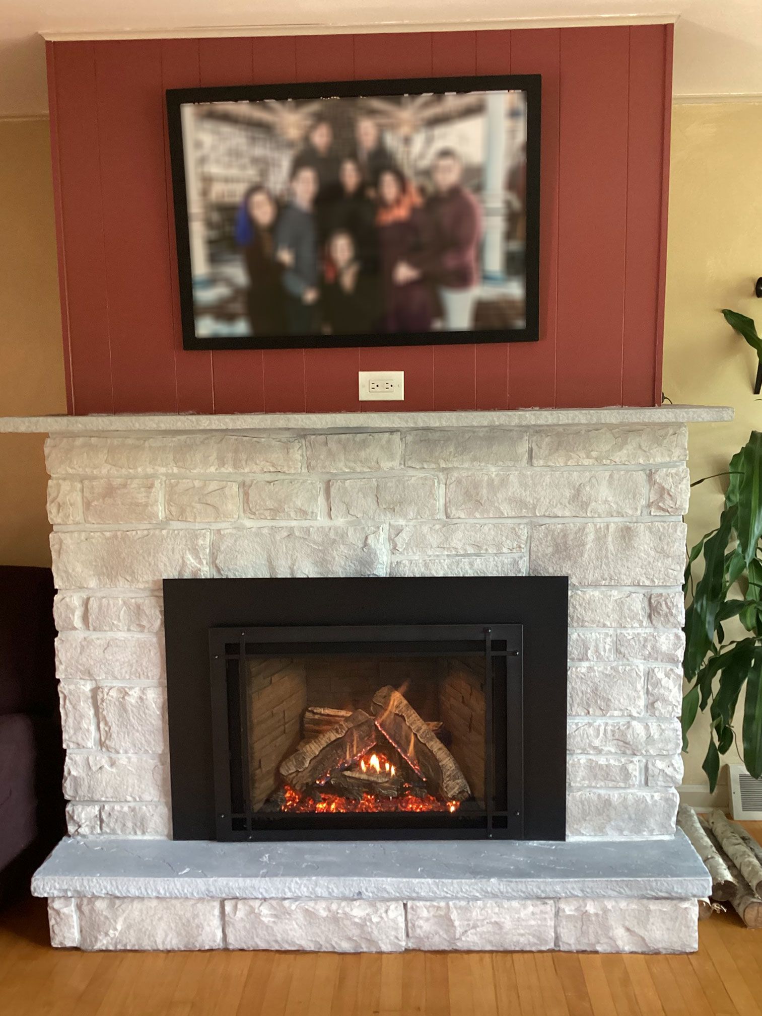 Fireplace with gray stone surround, fire burning, and family photo above on a red wall.