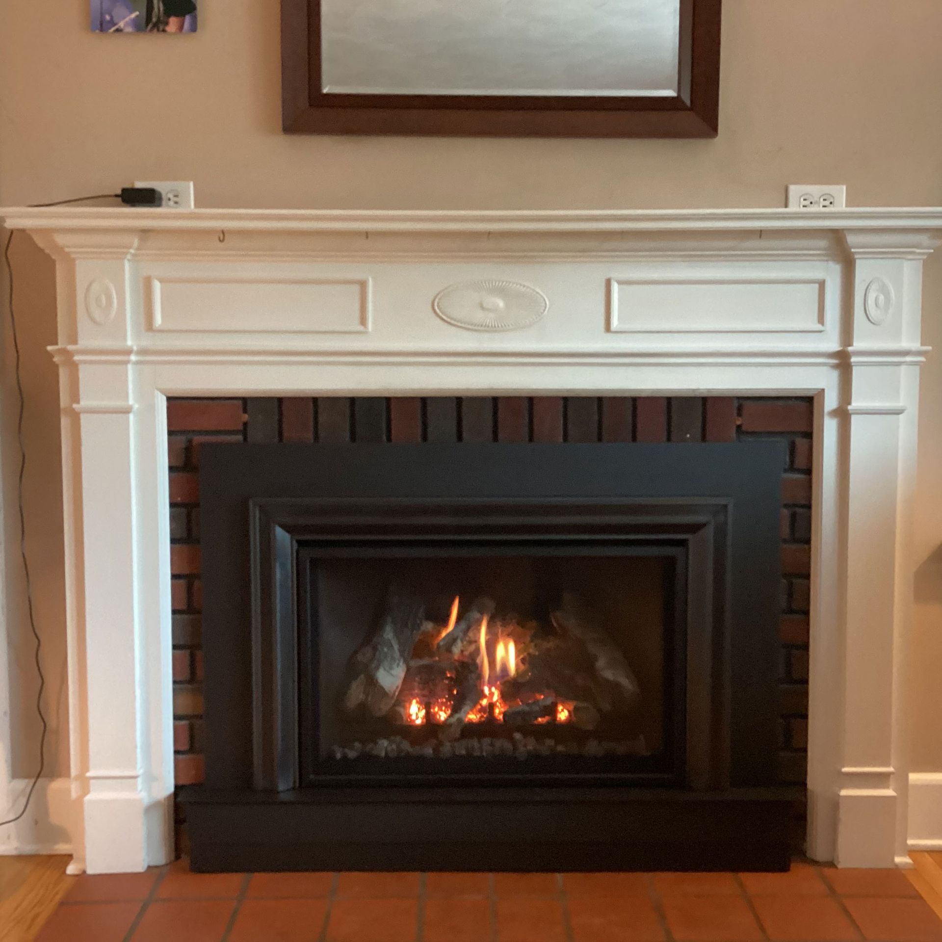 A fireplace with a white mantle and a lit fire, set against a brick backdrop, and an adjacent wood floor.