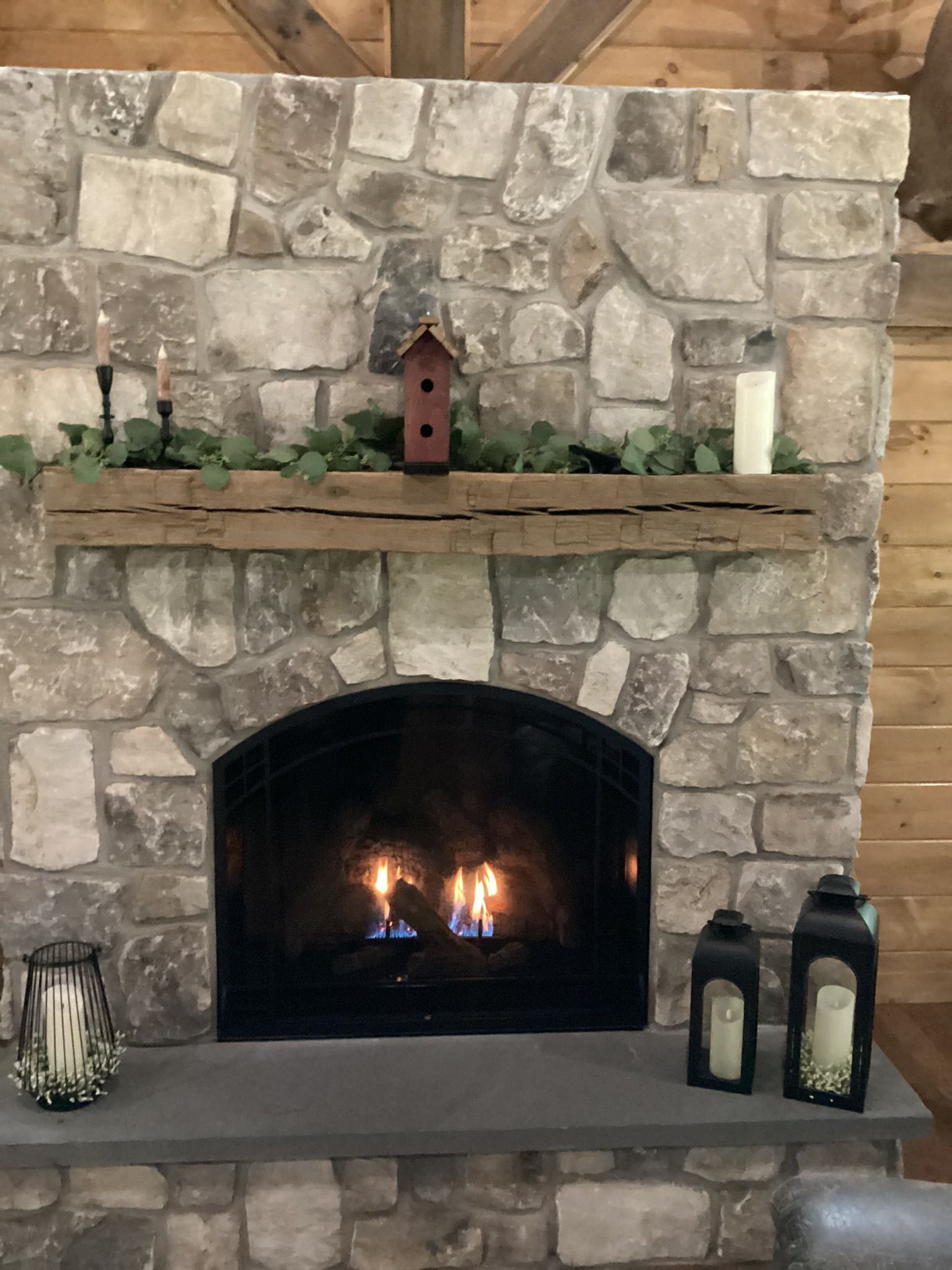 Stone fireplace with lit fire, wood mantel, candles, and lanterns.