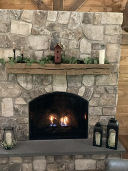 Stone fireplace with lit flames, wooden mantel, candles, and decorative birdhouse.