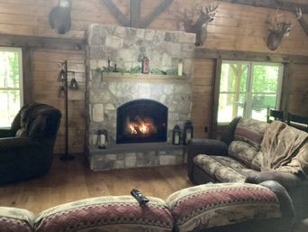 Cozy living room with stone fireplace, burning fire, deer heads mounted on logs, and two couches.