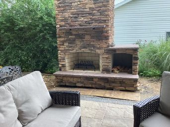 Outdoor stone fireplace with a wood storage compartment, surrounded by patio furniture.