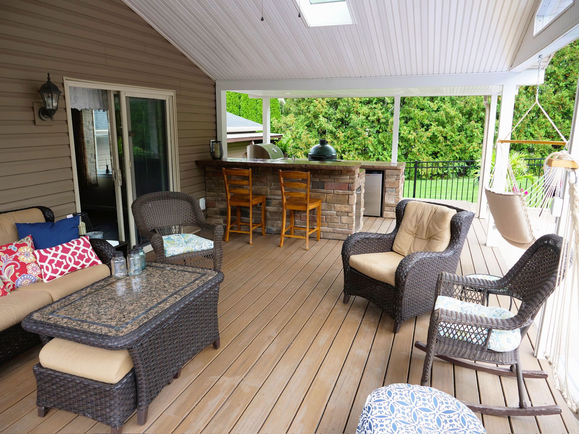 Covered wooden deck with outdoor furniture, bar, and hammock overlooking a green yard.