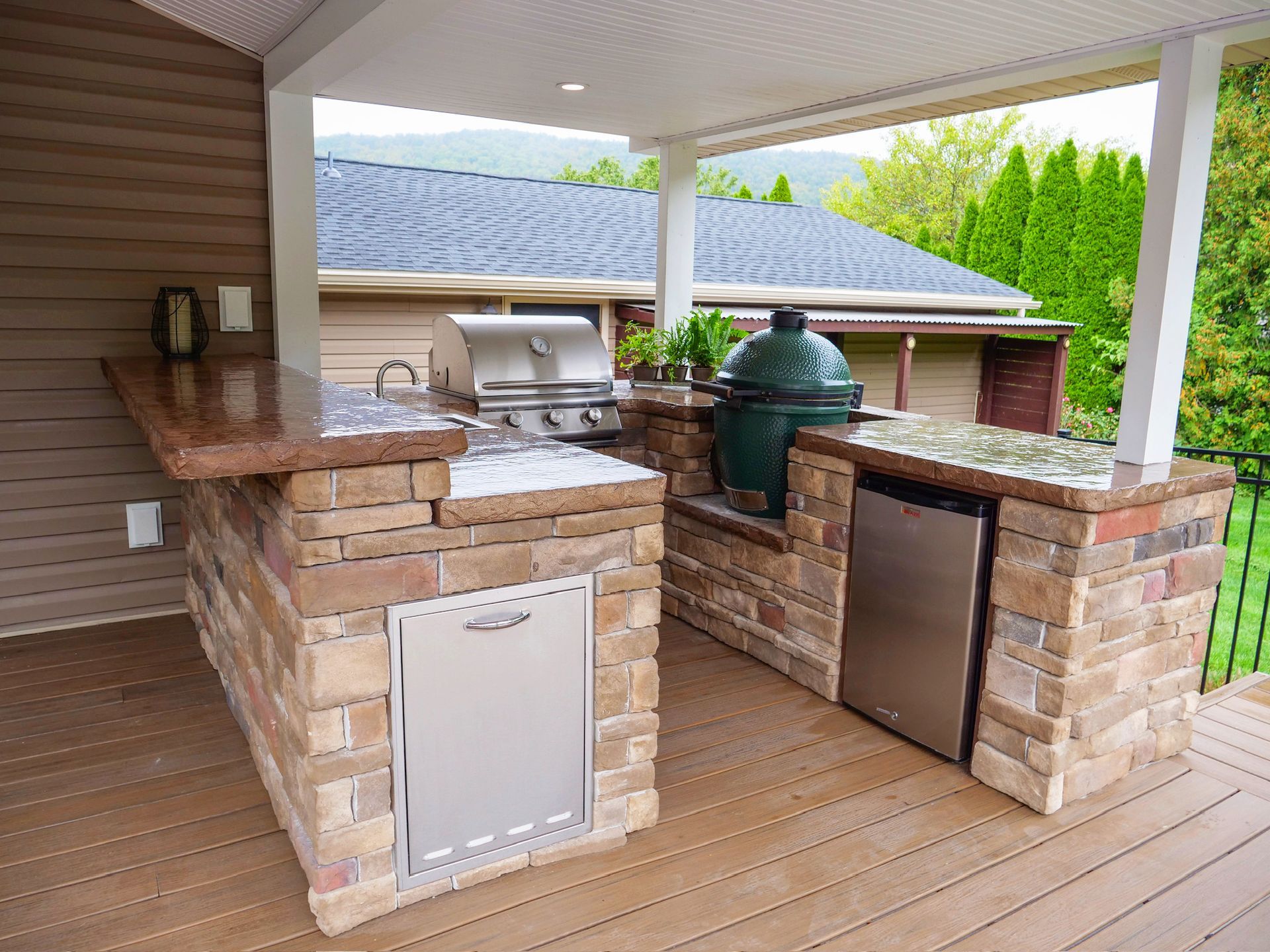 Outdoor kitchen on a deck with a grill, Big Green Egg, counter, and refrigerator.