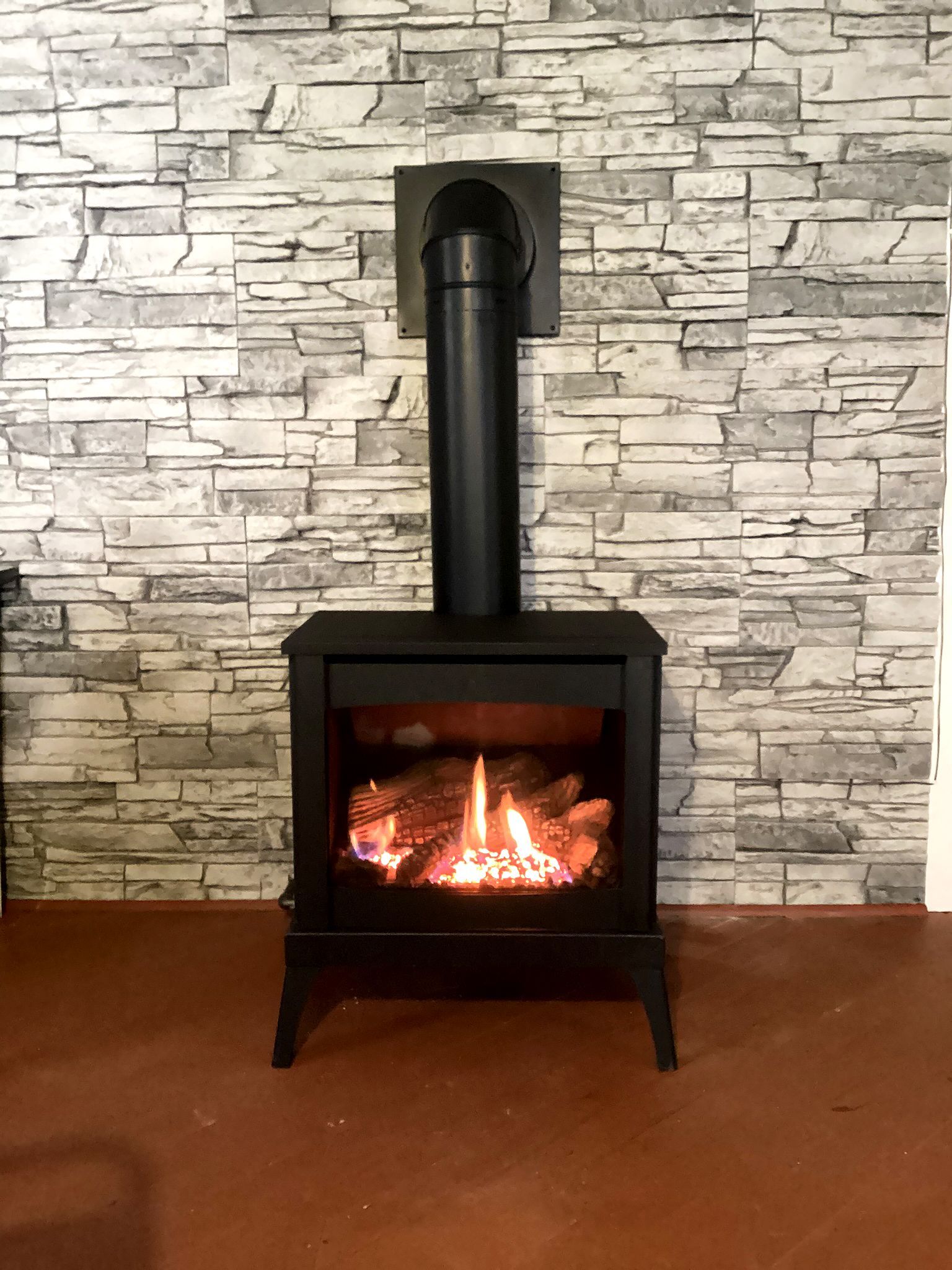 Black fireplace with flames against a brick-patterned wall.