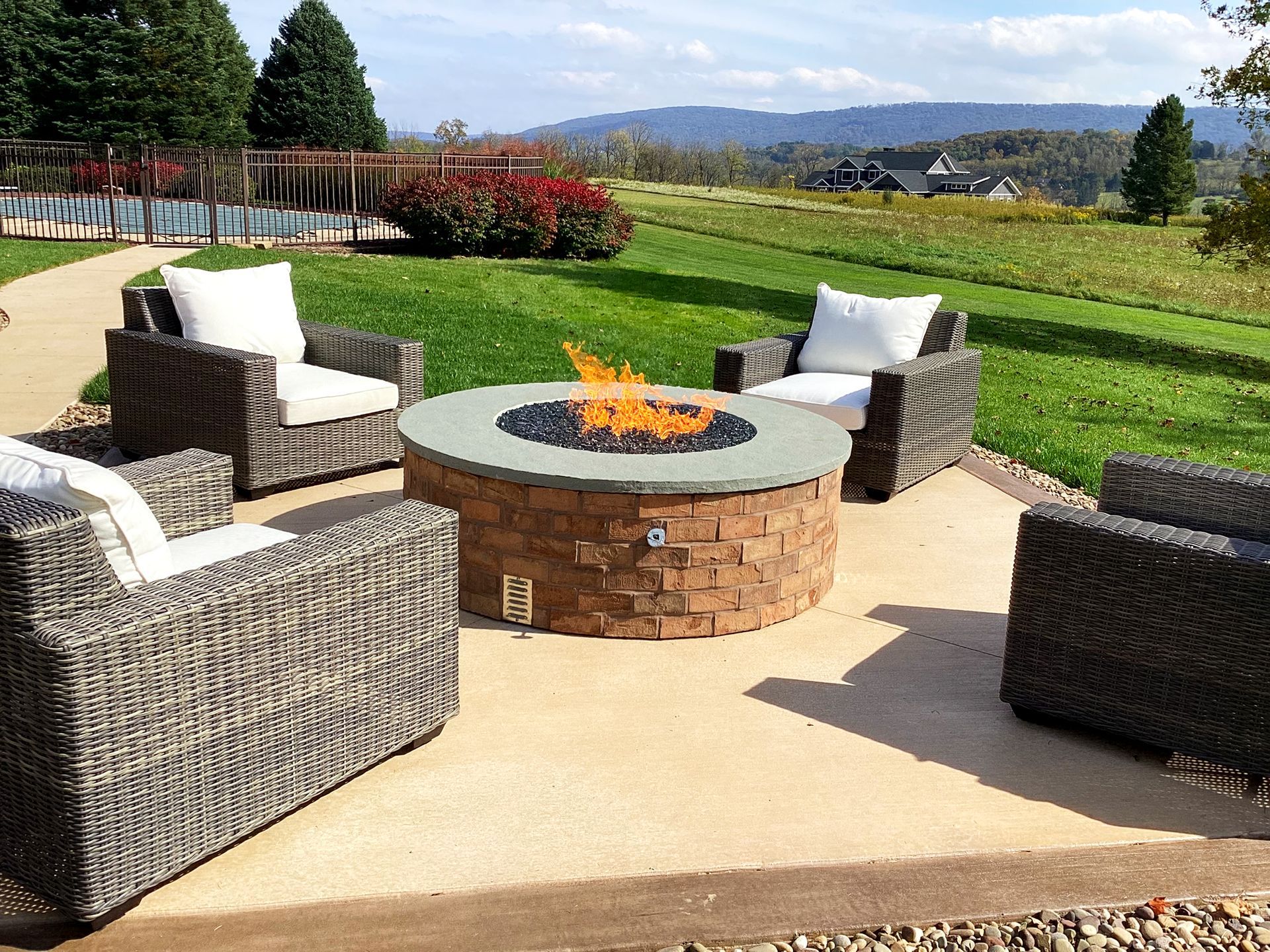 A cozy outdoor seating area with a fire pit, surrounded by chairs, grass, and a scenic view.