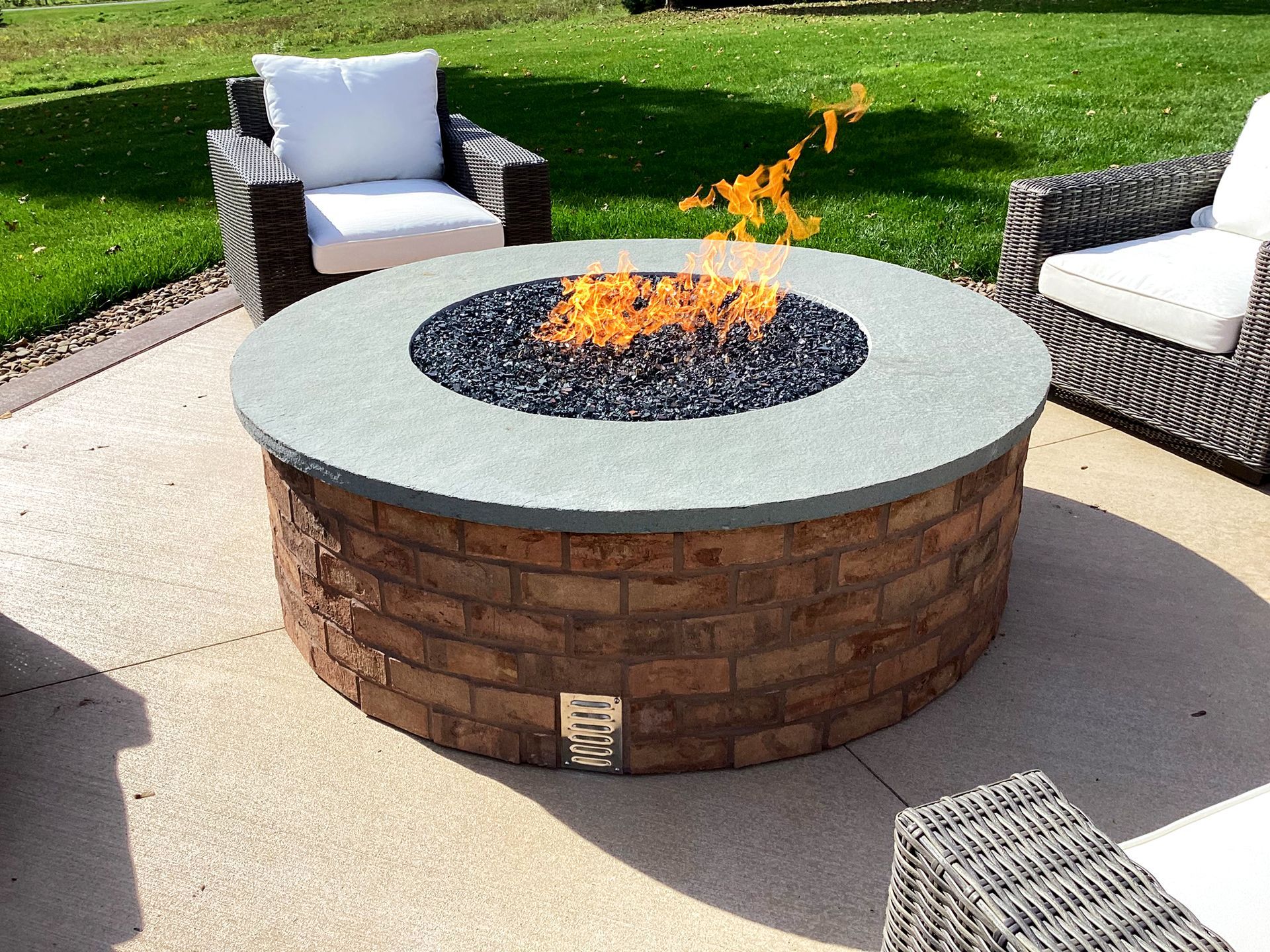 Fire pit with a brick exterior, surrounded by seating on a patio. Flames burn brightly.