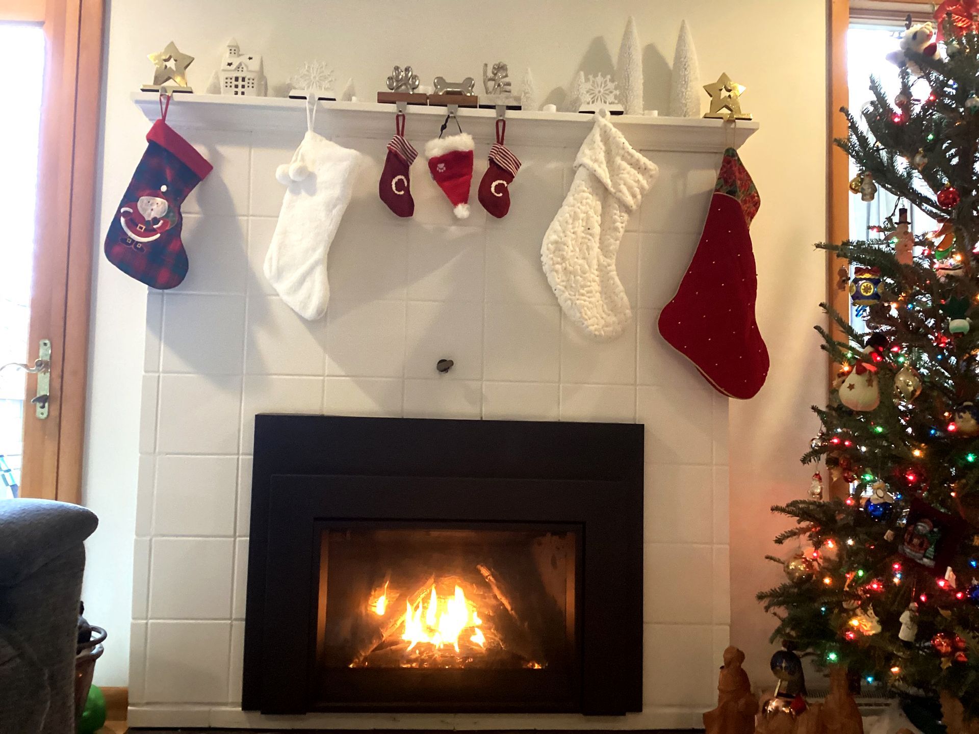 Fireplace with burning fire, decorated mantel with stockings, Christmas tree on right.