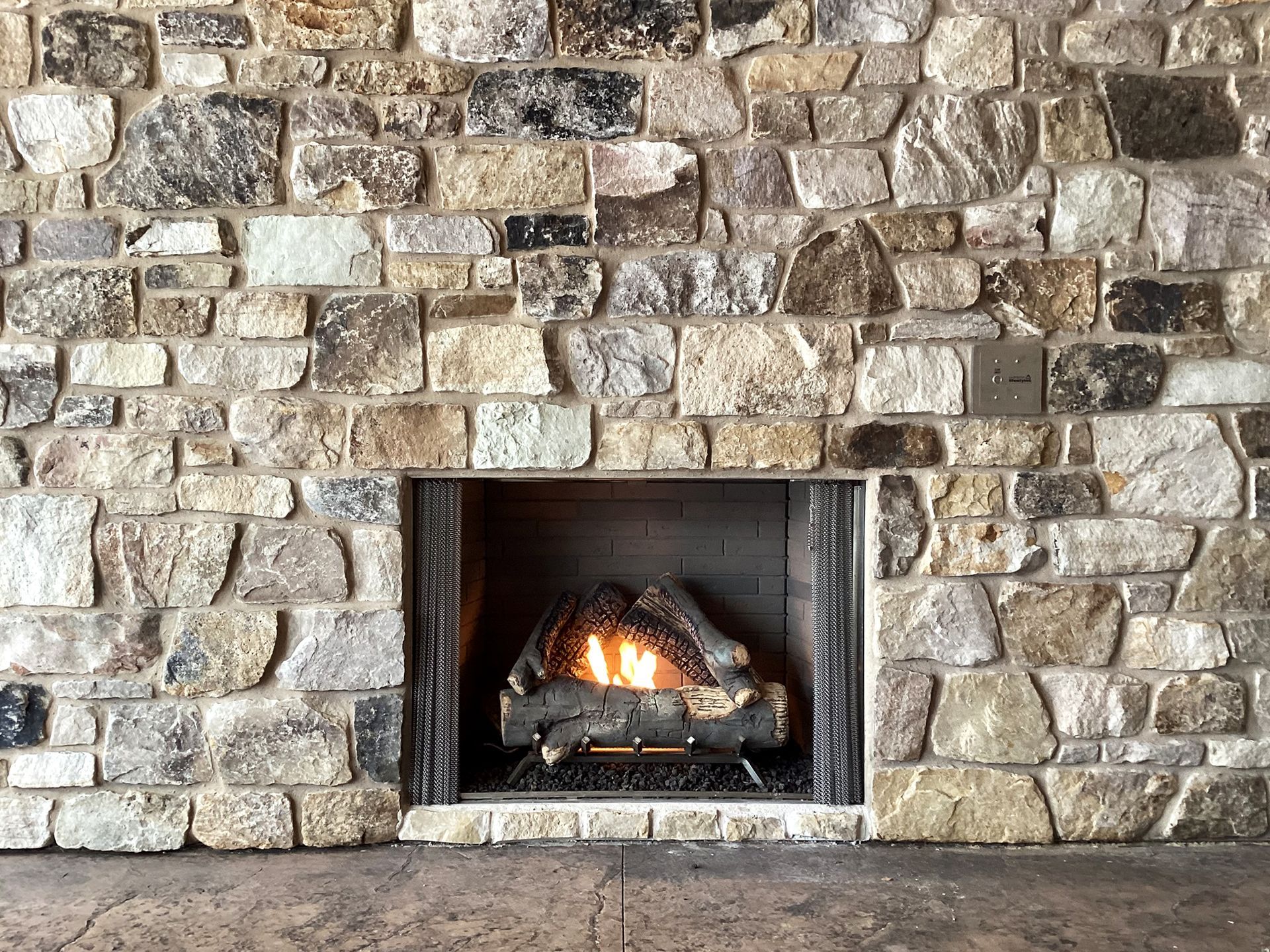 Fireplace with burning logs, set within a stone wall with varying neutral tones.