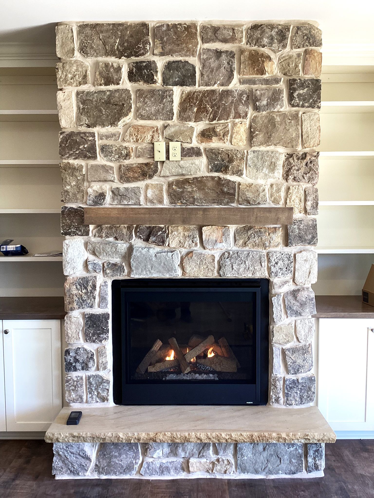 Stone fireplace with a lit fire, flanked by built-in bookshelves and white cabinets.