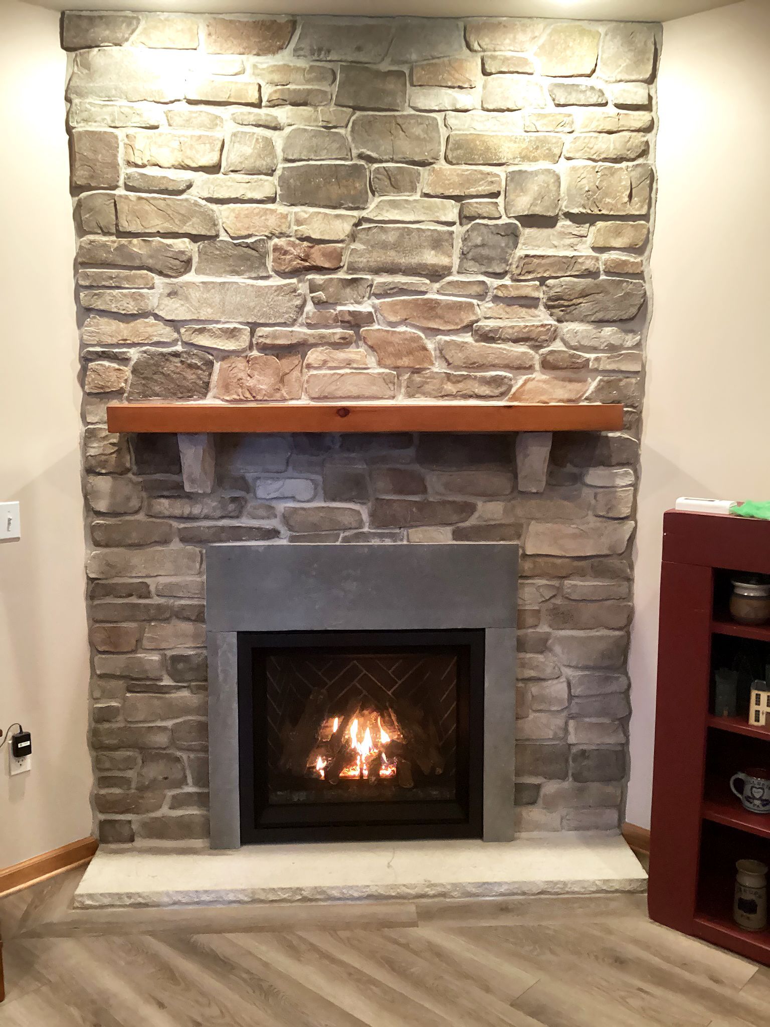 Stone fireplace with a burning fire, wooden mantel, and gray hearth.