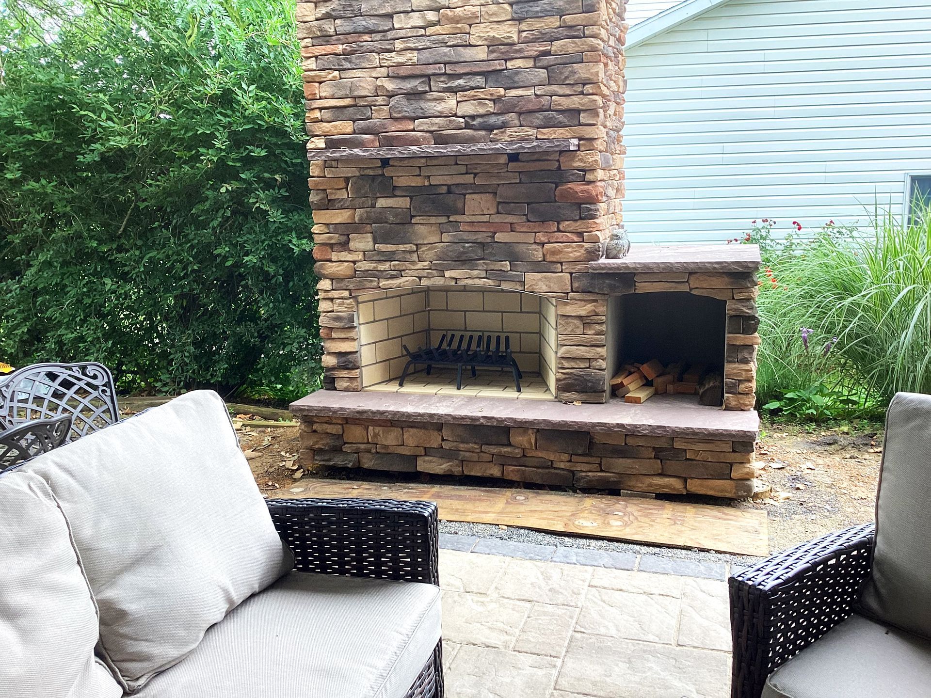 Outdoor fireplace with a stacked stone facade; wicker furniture on a patio.