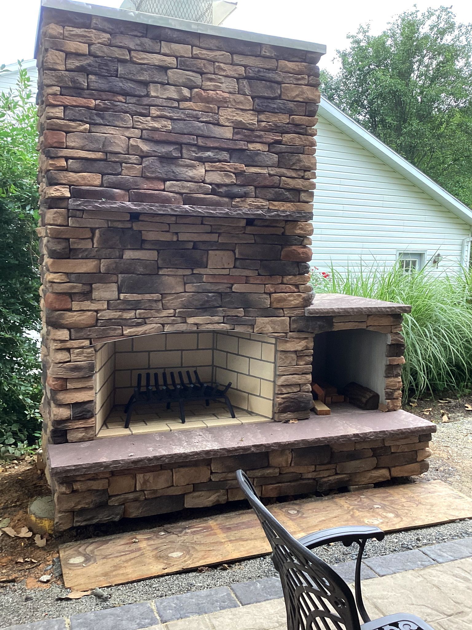 Stone outdoor fireplace with brick firebox, wood storage, and metal grate.