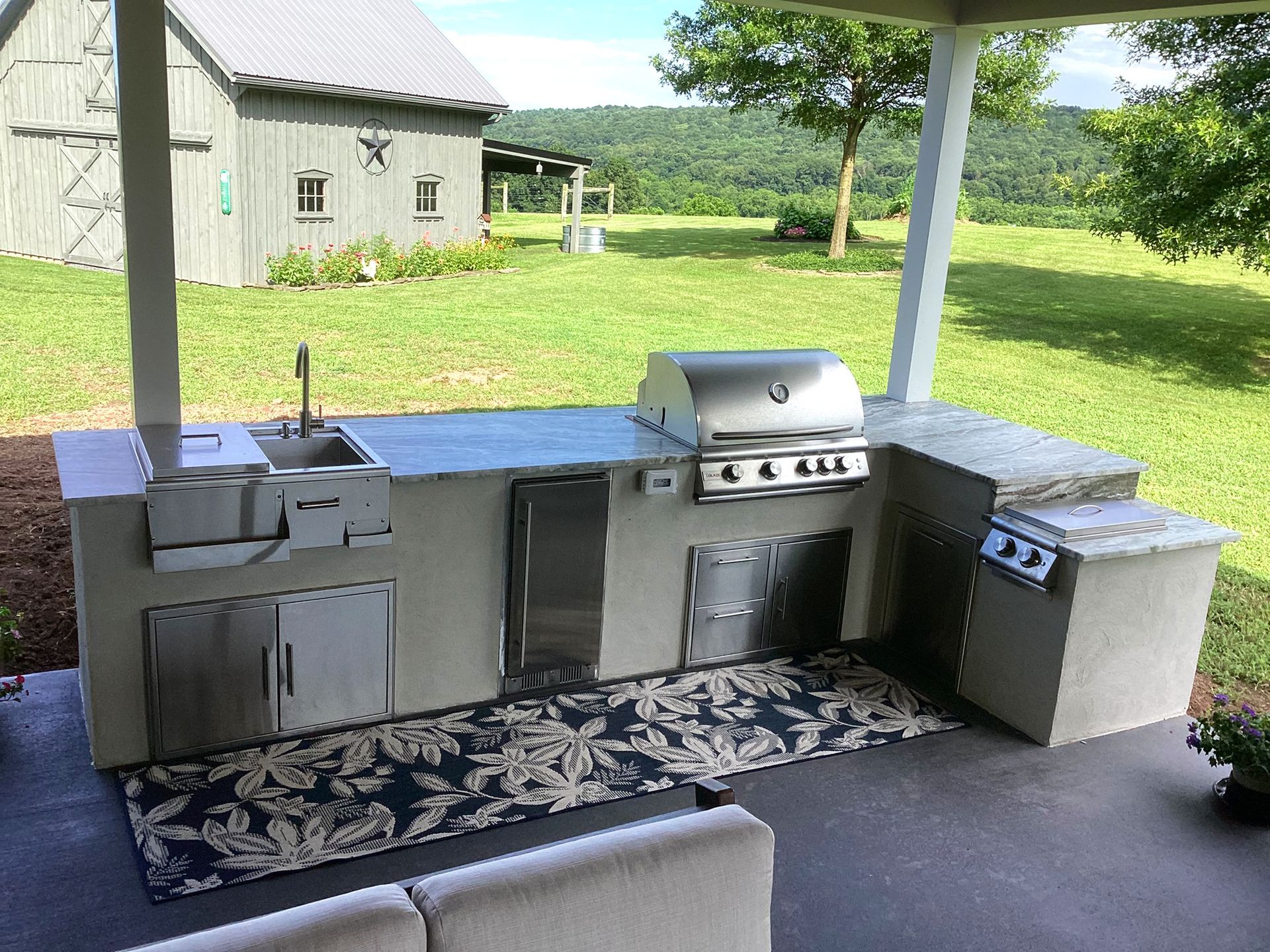 Outdoor kitchen with a grill, sink, and stainless steel doors under a covered patio.