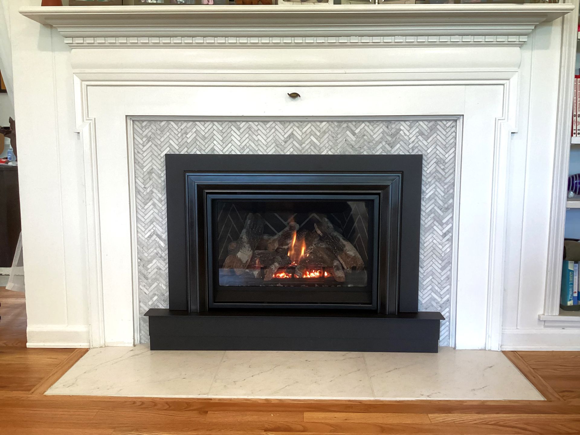 Fireplace with a black frame and herringbone tile surround, set in a white mantel.