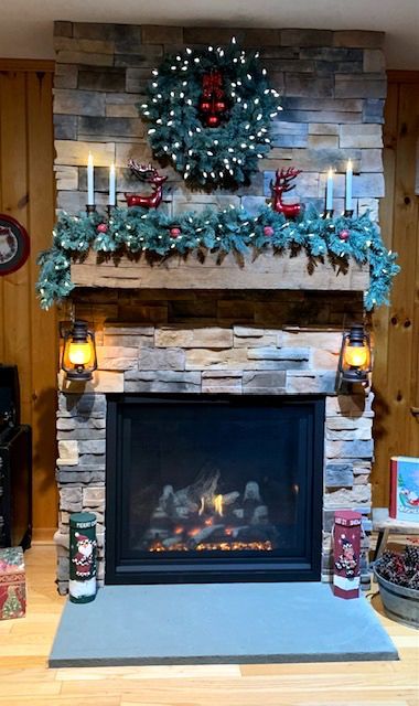A fireplace with Christmas decorations: a wreath, garland, candles, and Santa figures.