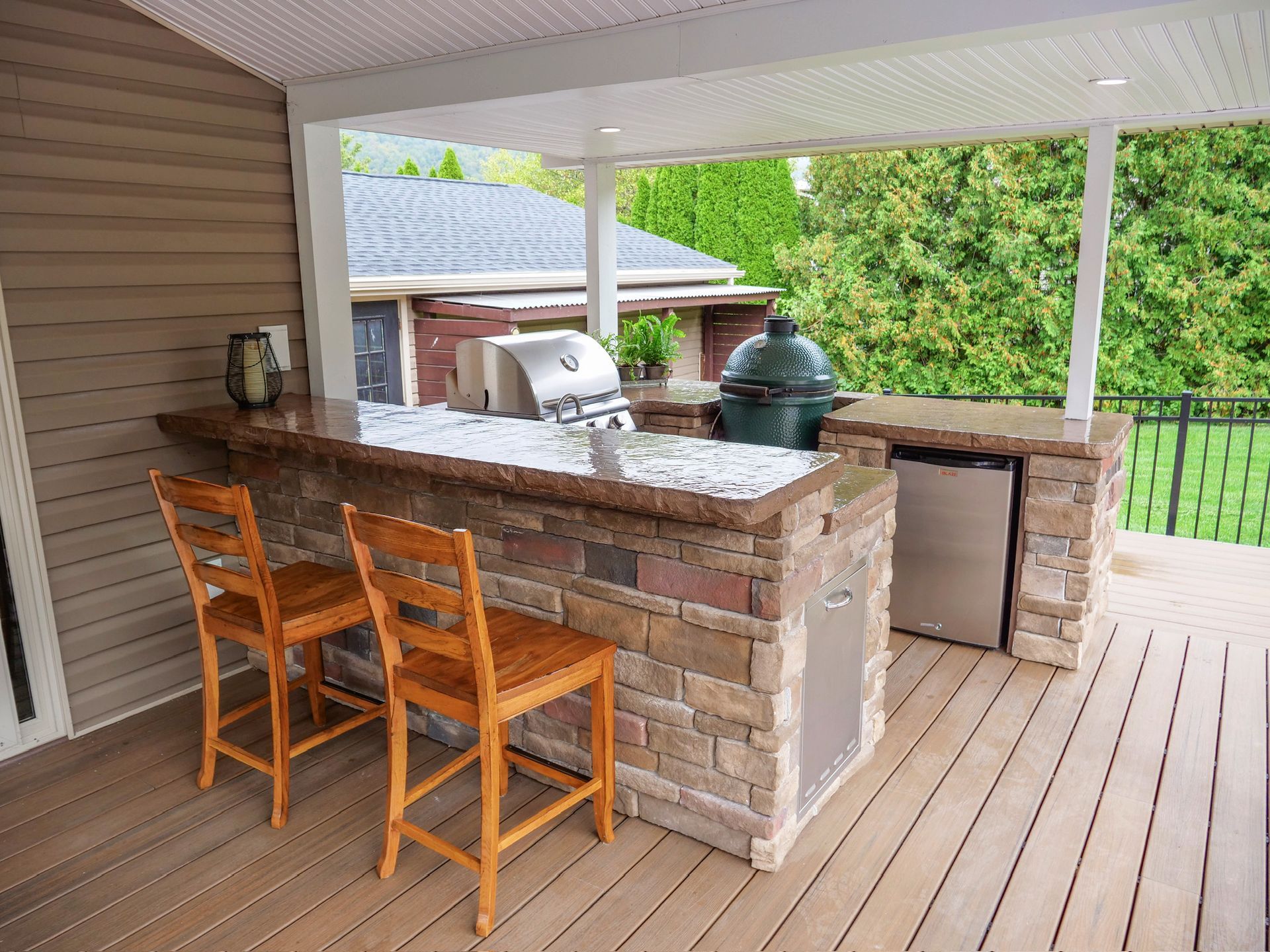 Outdoor kitchen with brick bar, grill, fridge, and seating on a deck.