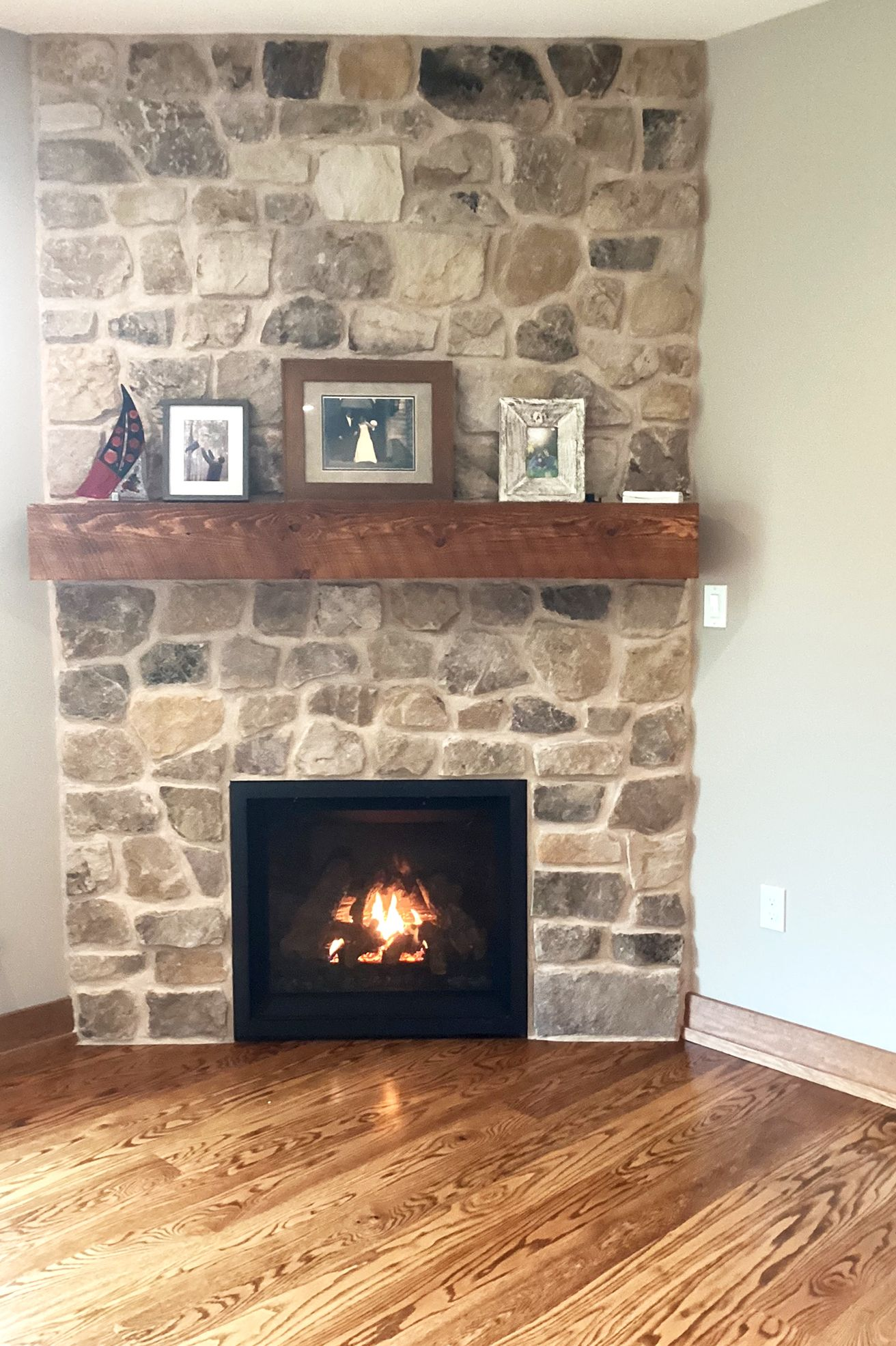Stone fireplace with a wooden mantel, lit fire, framed photos.