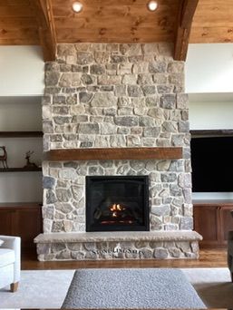 Stone fireplace with wooden mantel and beams, neutral colors, fire burning.