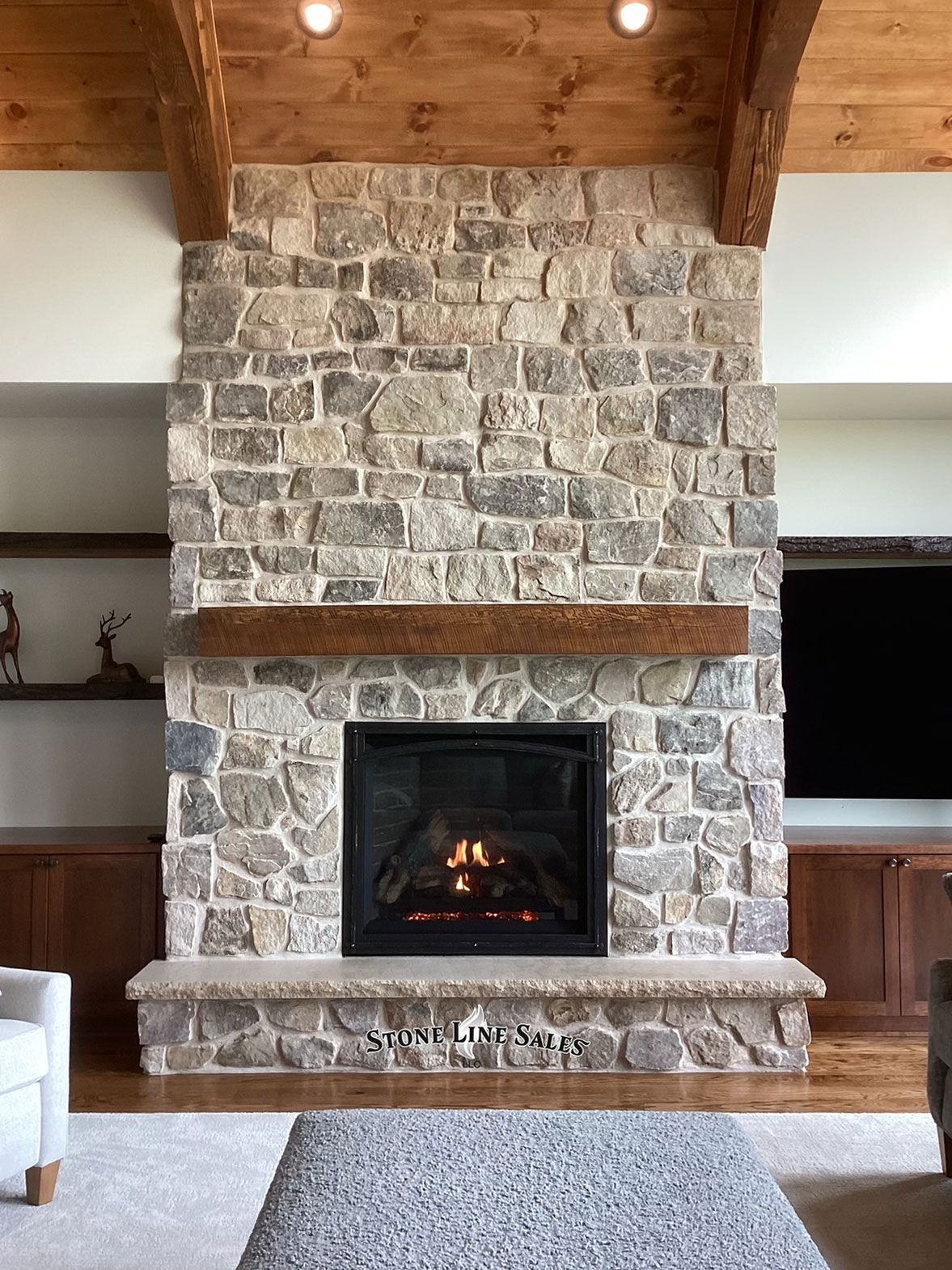 Stone fireplace with a wooden mantel, flanked by built-in cabinetry, in a living room.