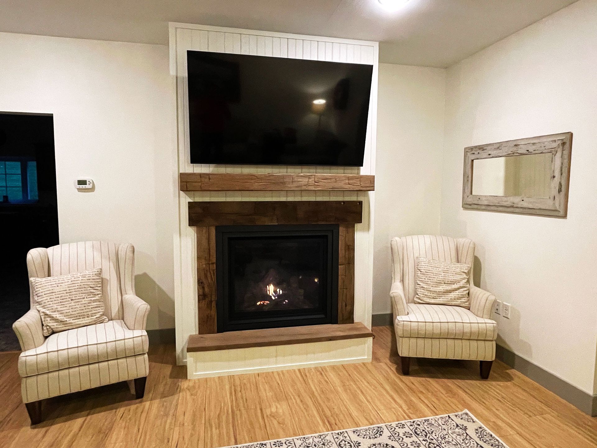 Cozy living room with fireplace, TV, two armchairs, and a decorative mirror.