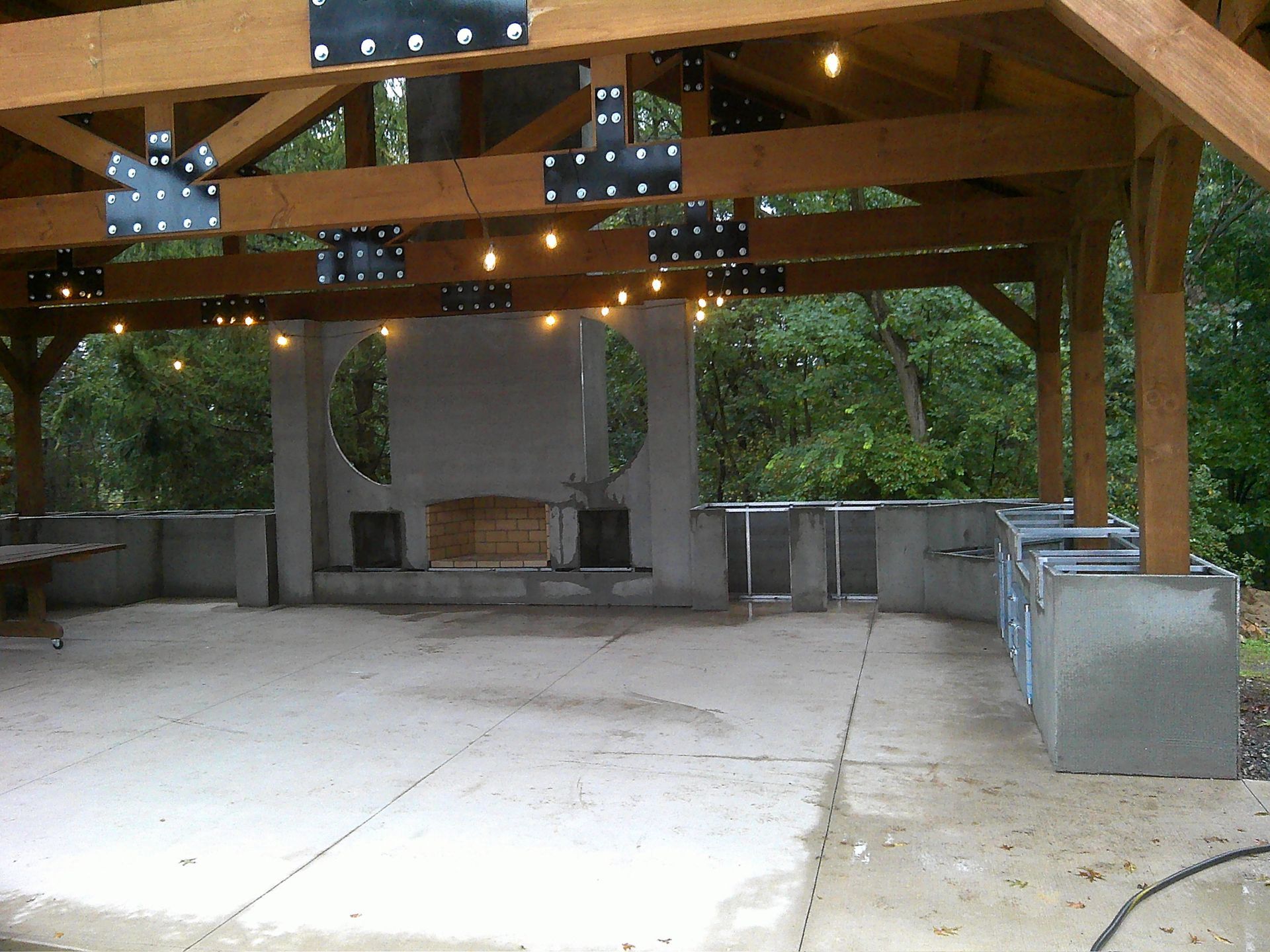 Outdoor patio with a concrete floor, fireplace, and wooden beams, with string lights.