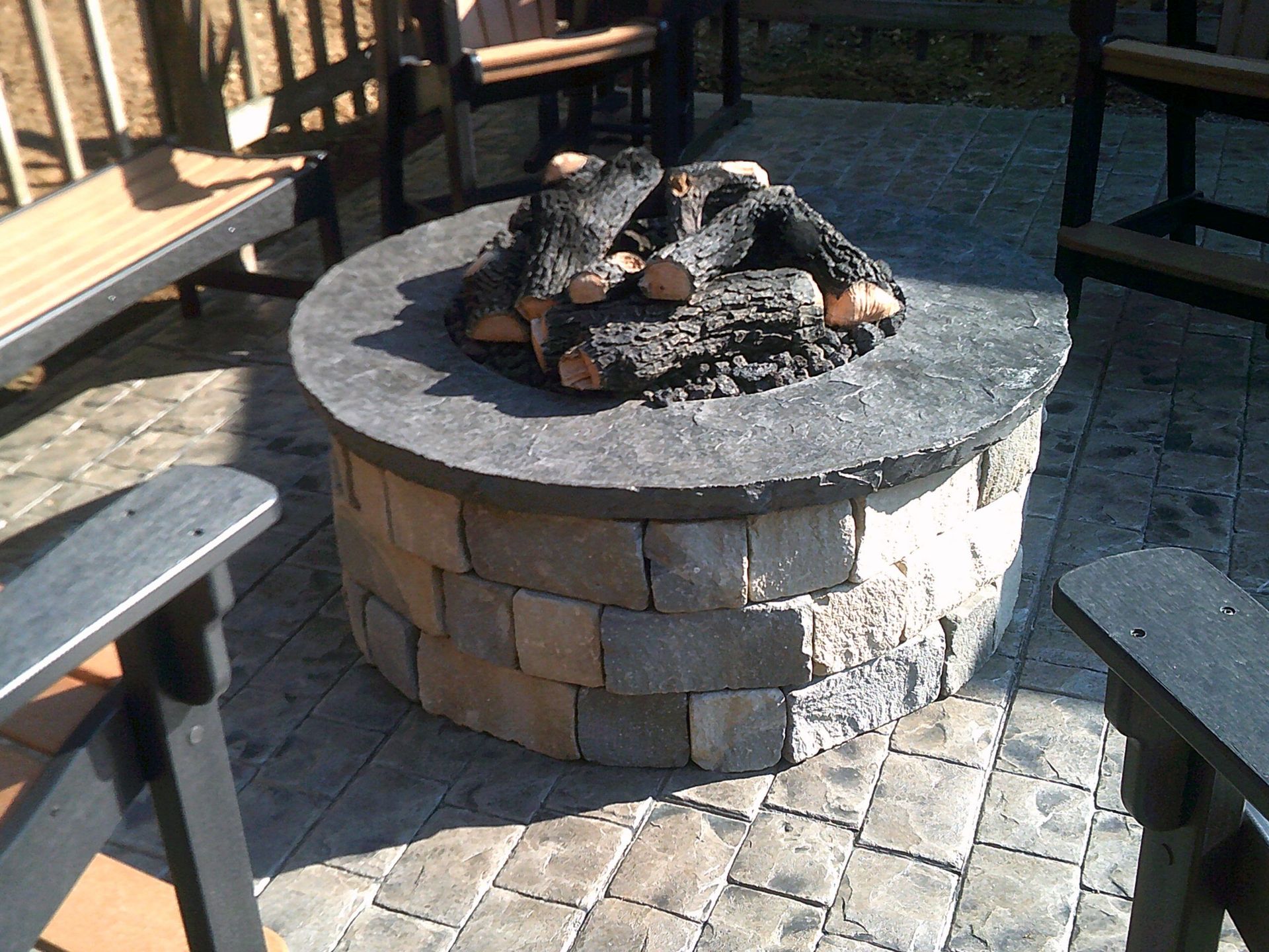 A fire pit with logs in it is surrounded by chairs