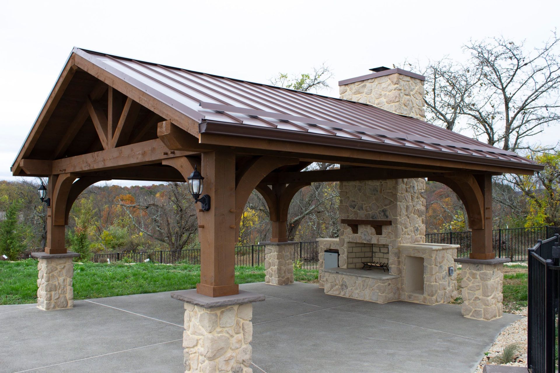 A wooden pavilion with a metal roof and a stone fireplace