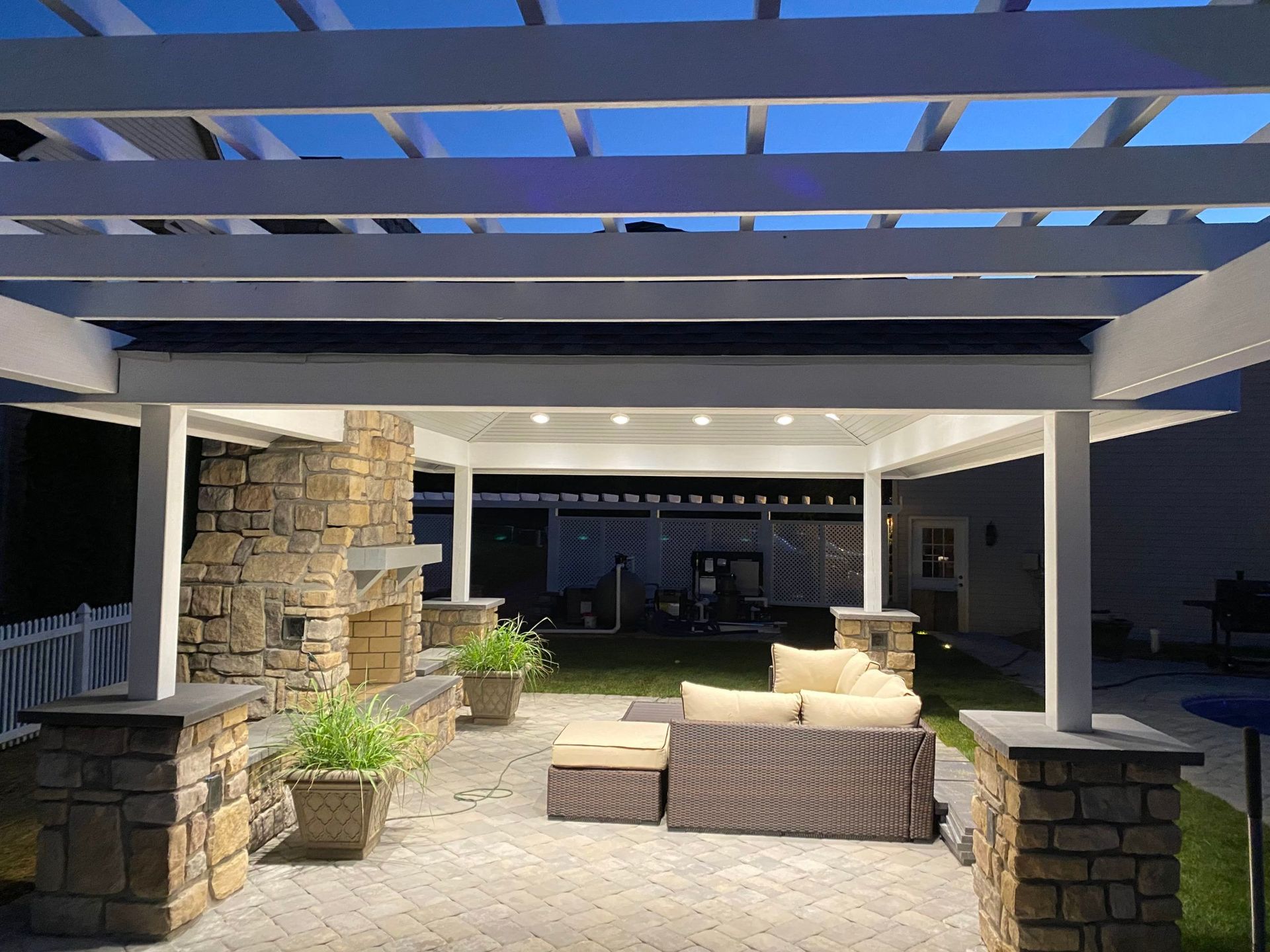 A patio with a pergola and a fireplace at night.