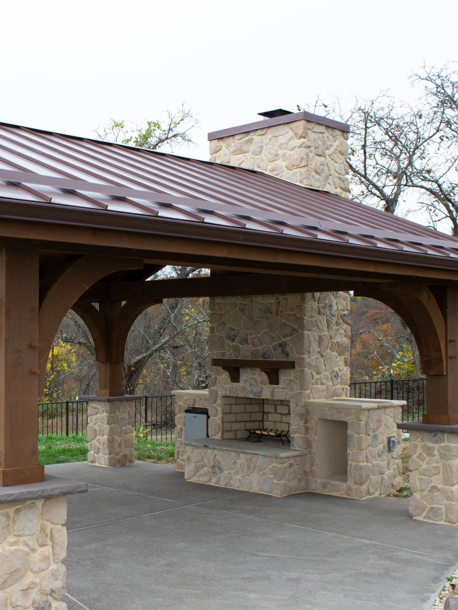 A stone fireplace under a wooden pavilion with a metal roof.
