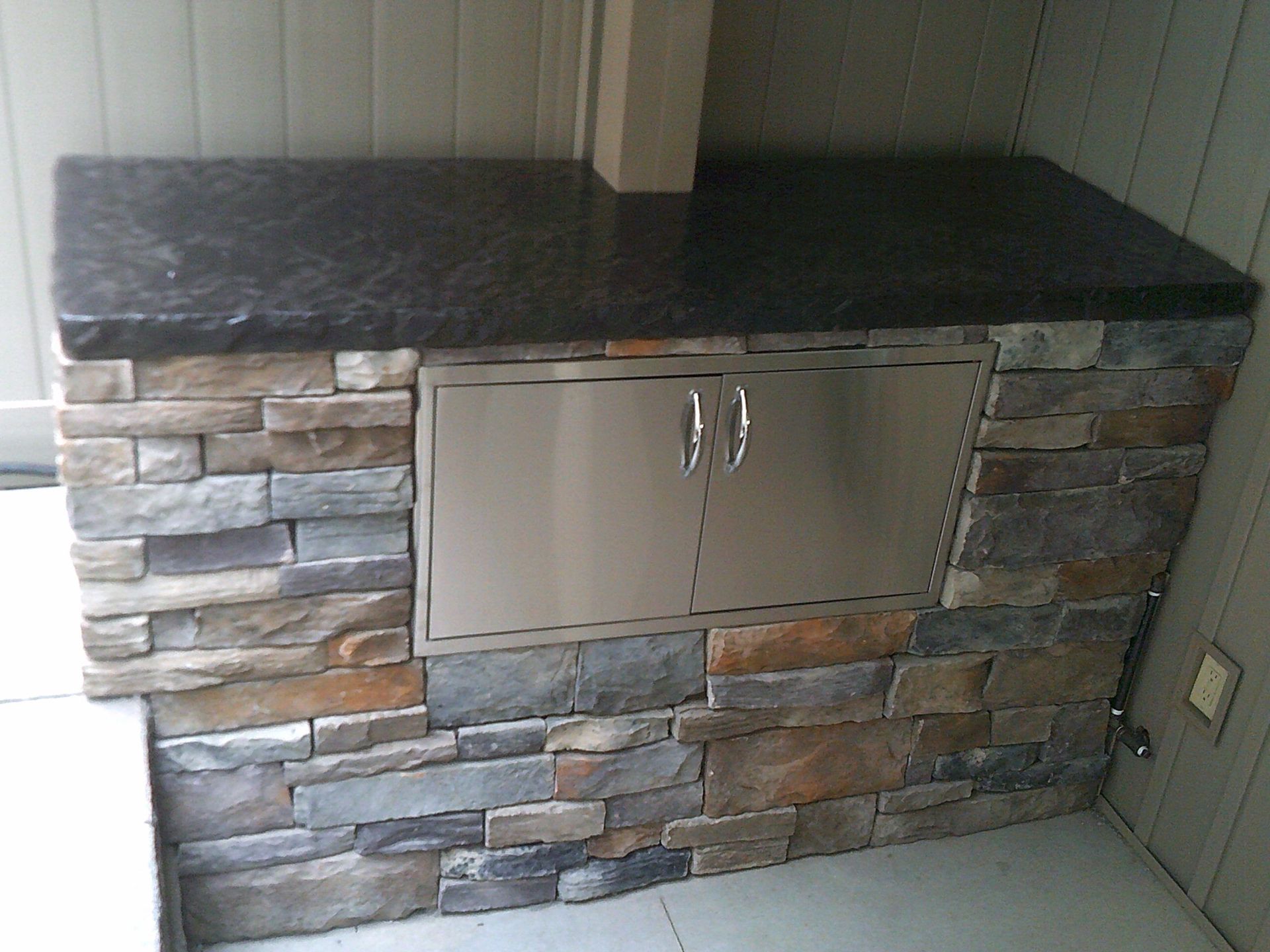 A stone wall with a black counter top and a stainless steel door.