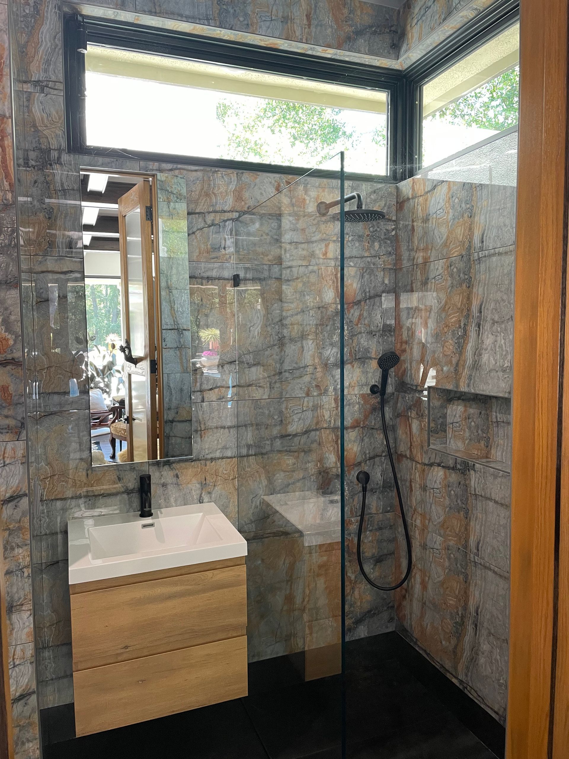 Modern bathroom with glass shower, floating sink, and dark tiled floor