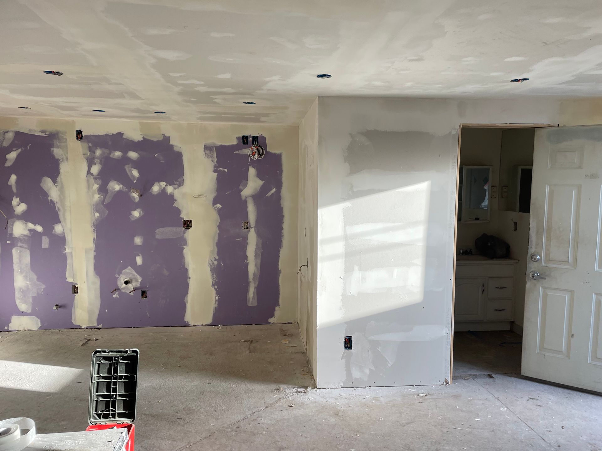 Partially renovated room with purple drywall patches, white wall, open door, and paint can on floor