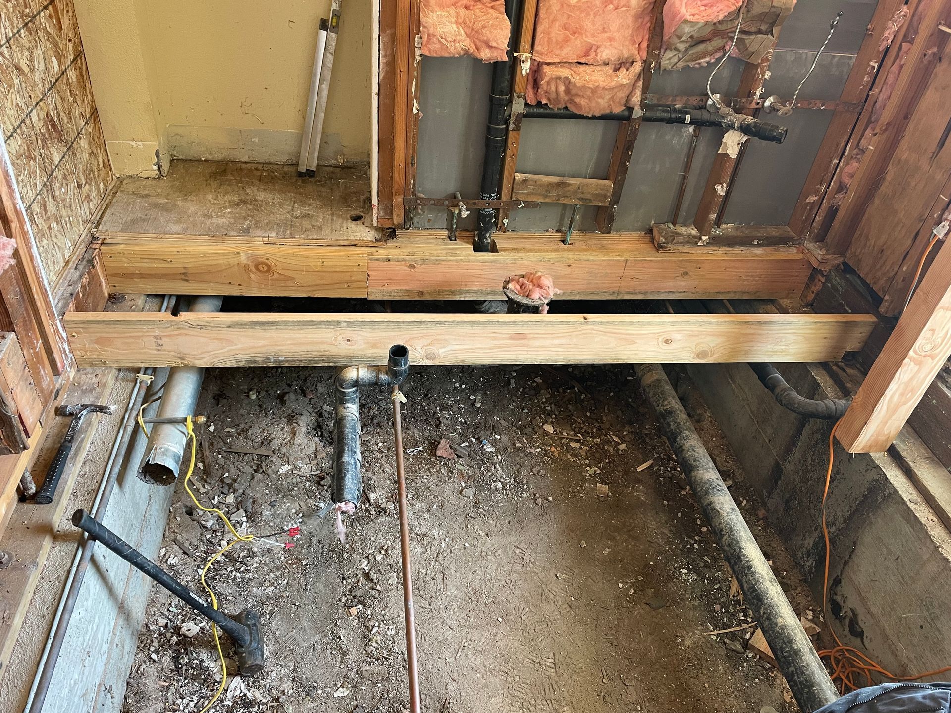 Exposed floor joists and pipes inside a damaged, partially demolished room floor