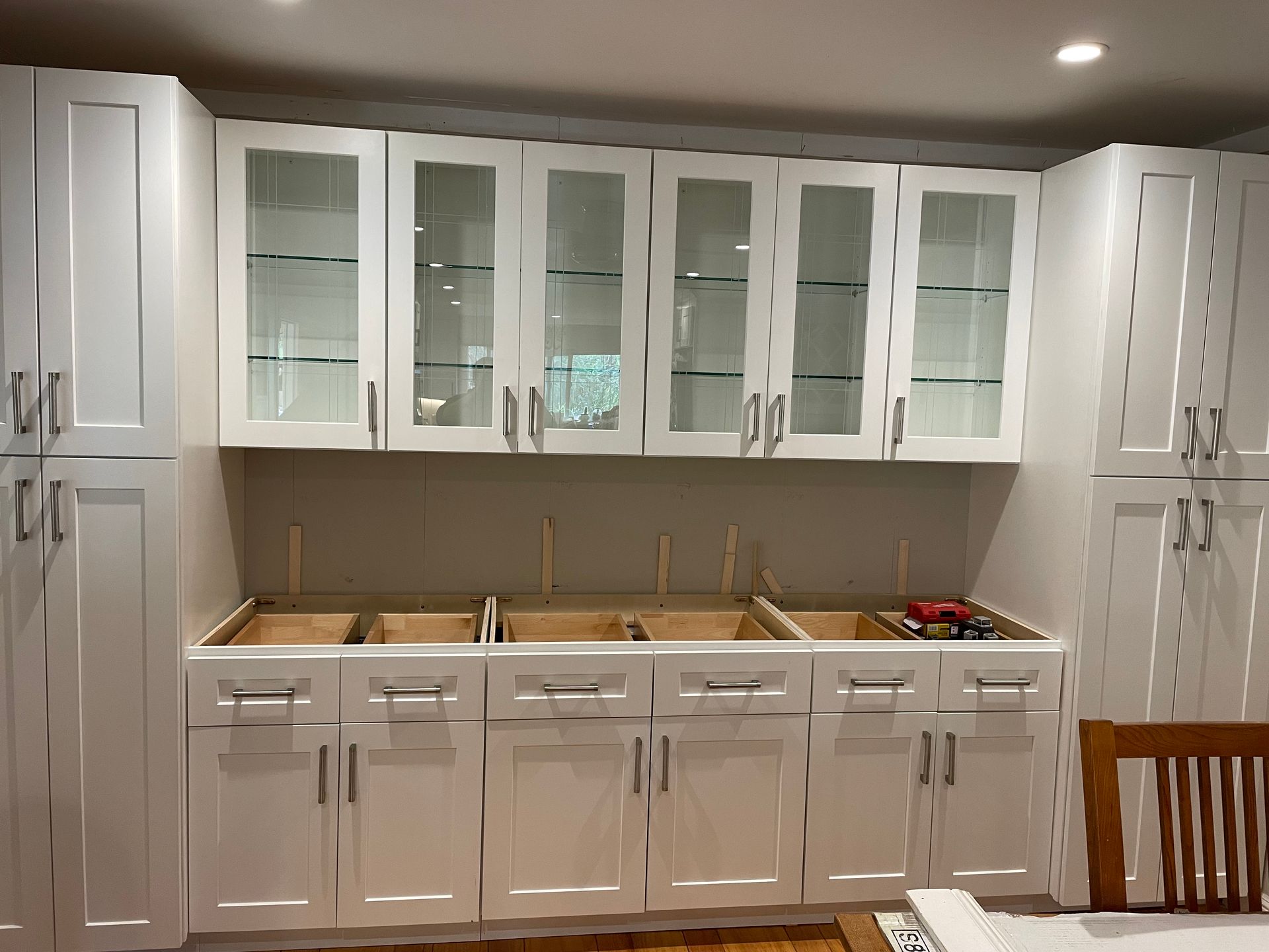 White kitchen cabinets with glass fronts and a countertop against a dark wall.
