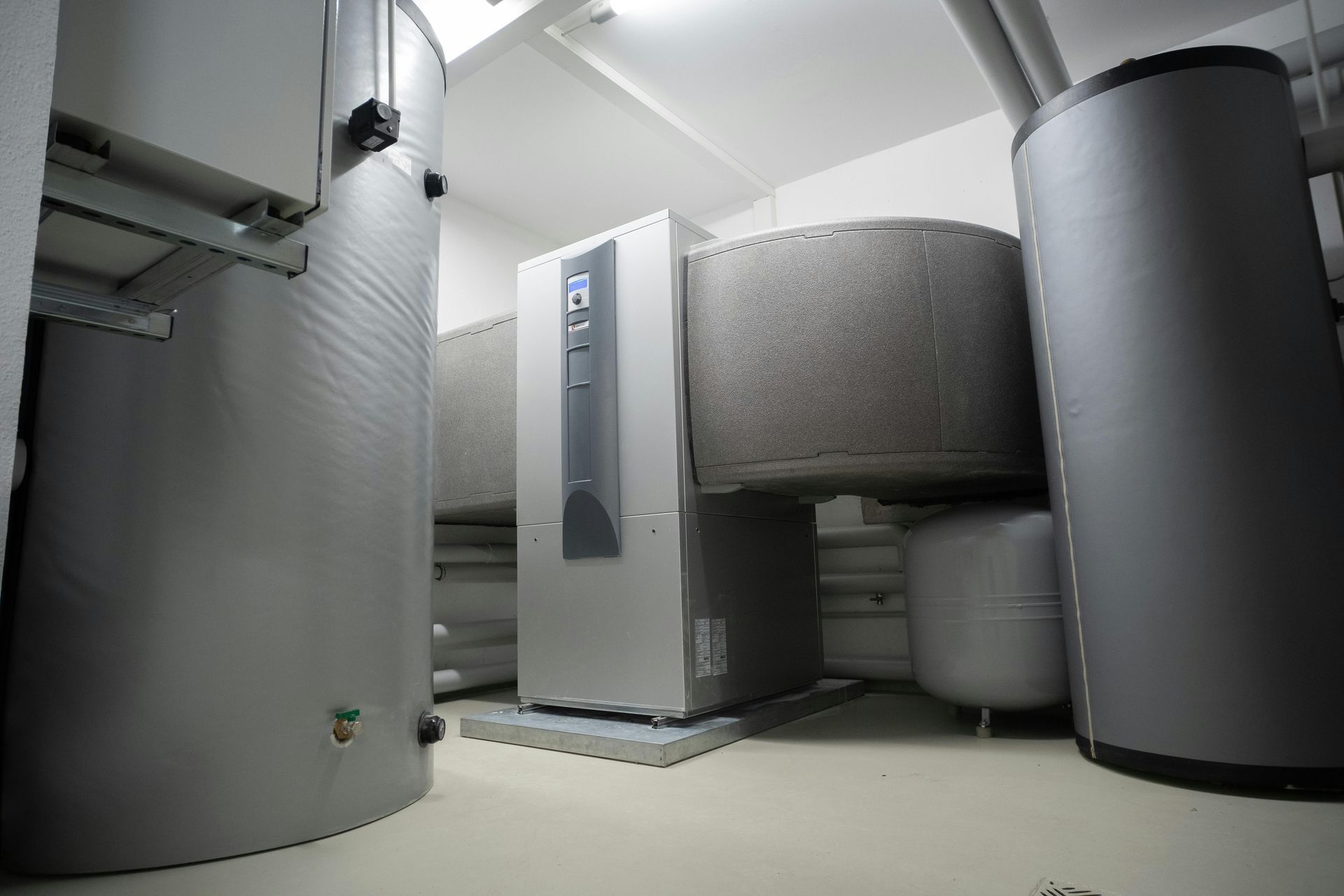 Industrial boiler room with large gray tanks and a central heating unit.