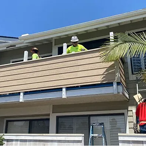 Construction workers on a balcony, installing siding, sunny day.