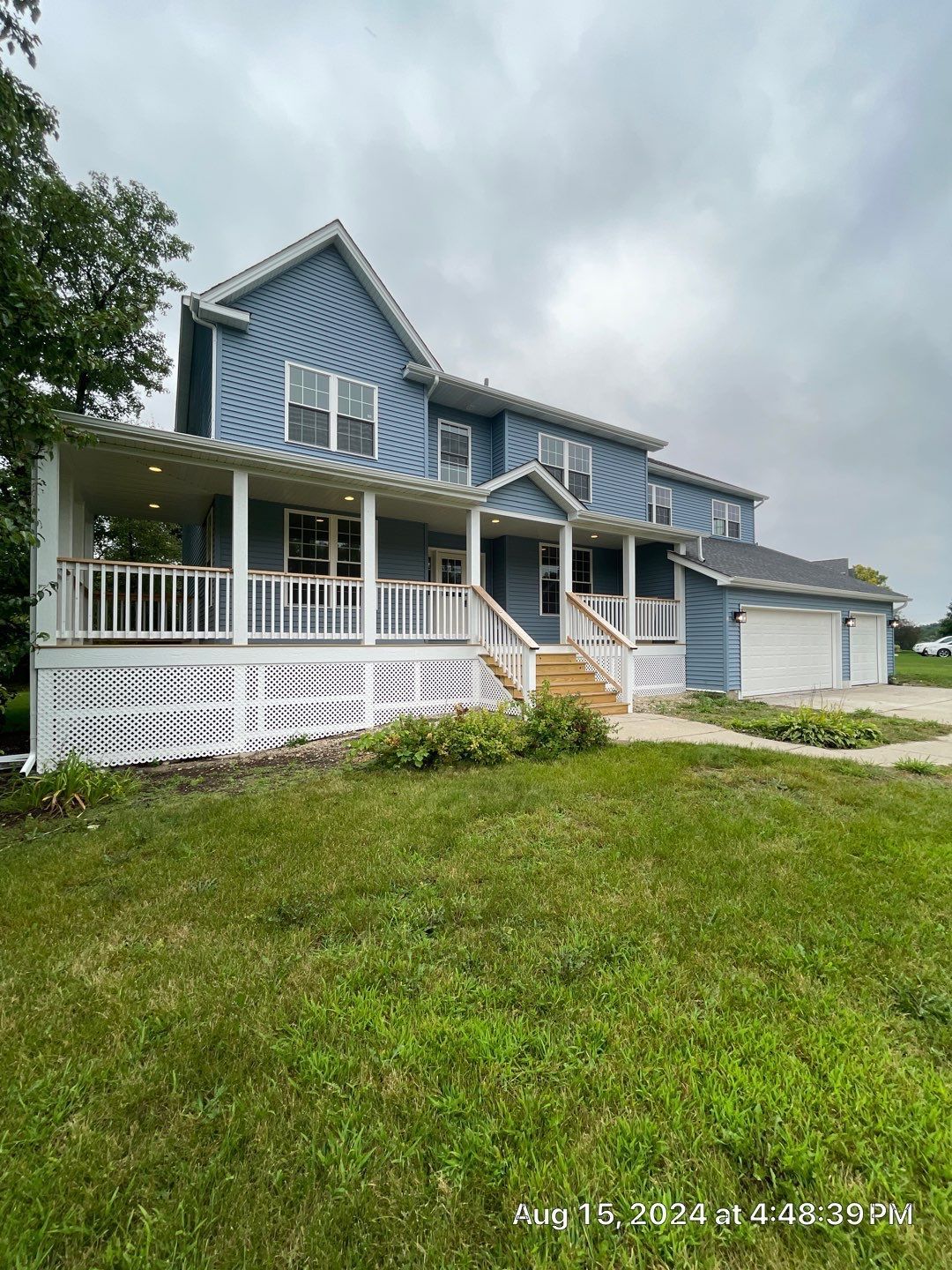A large blue house with a large porch and stairs is sitting on top of a lush green field.