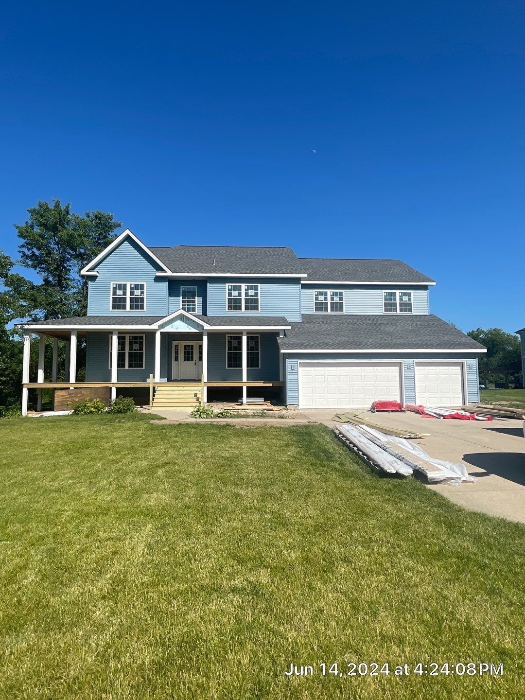 Two-story blue house under construction with a porch and two-car garage on a grassy lawn.