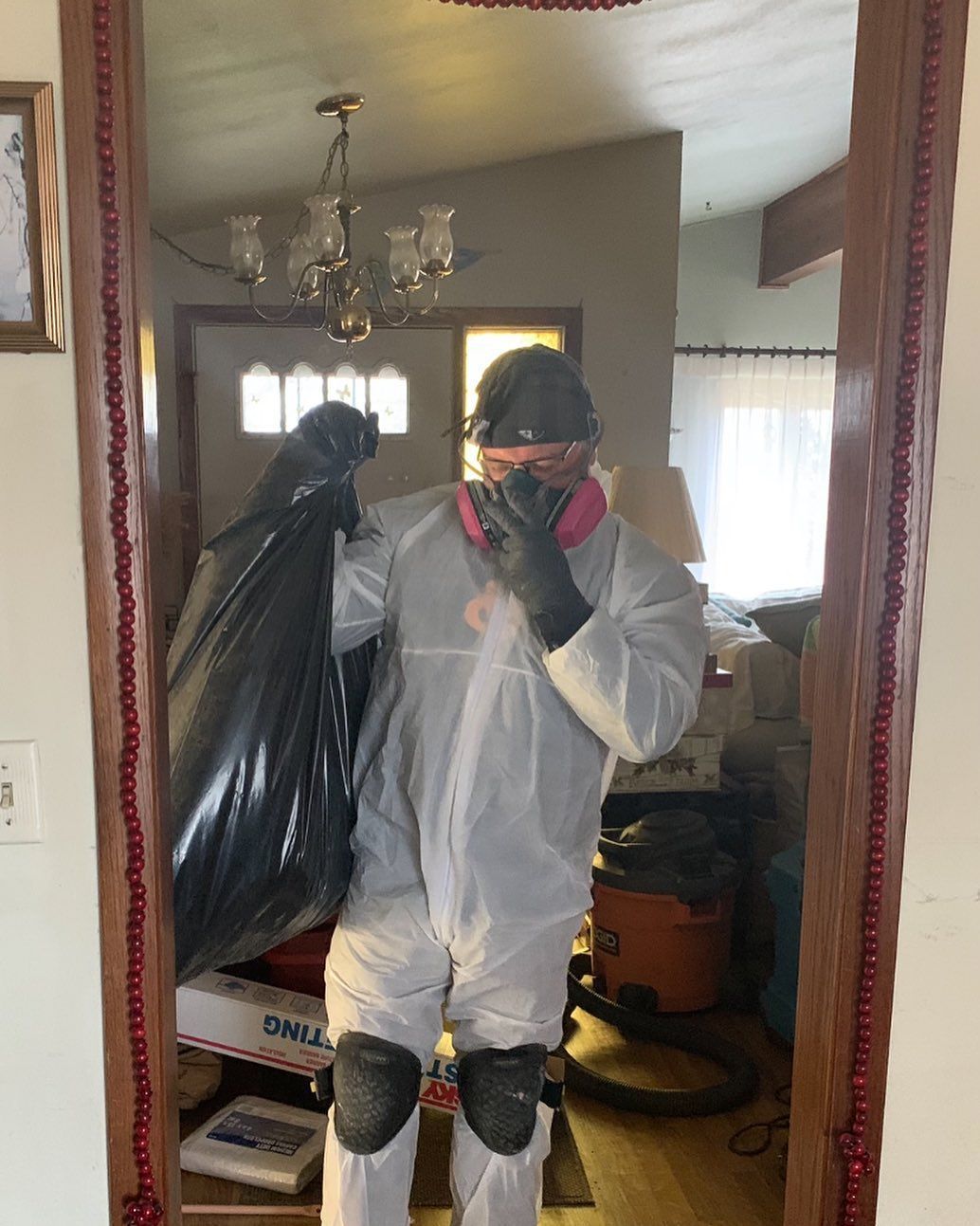 A man in a protective suit is holding a bag in front of a mirror.