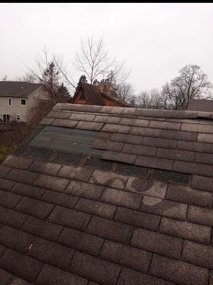 A roof with a lot of shingles on it and a house in the background.