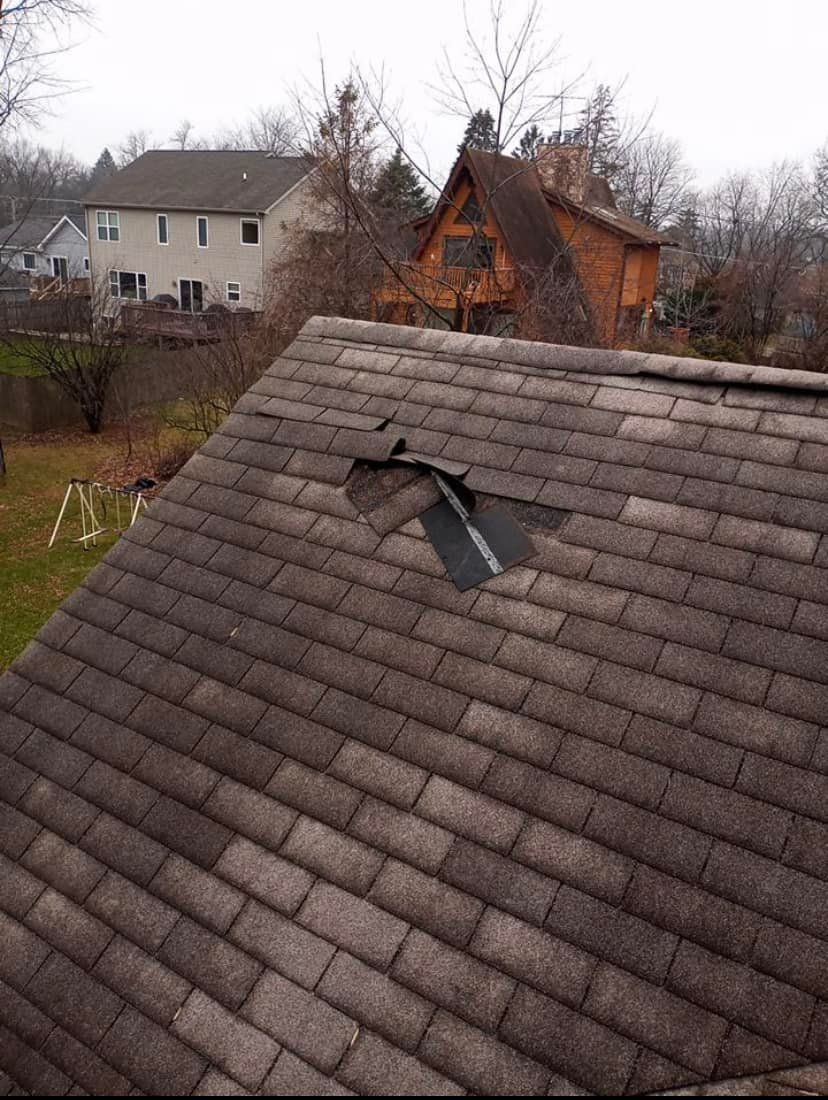 A roof with a hole in it and a house in the background.