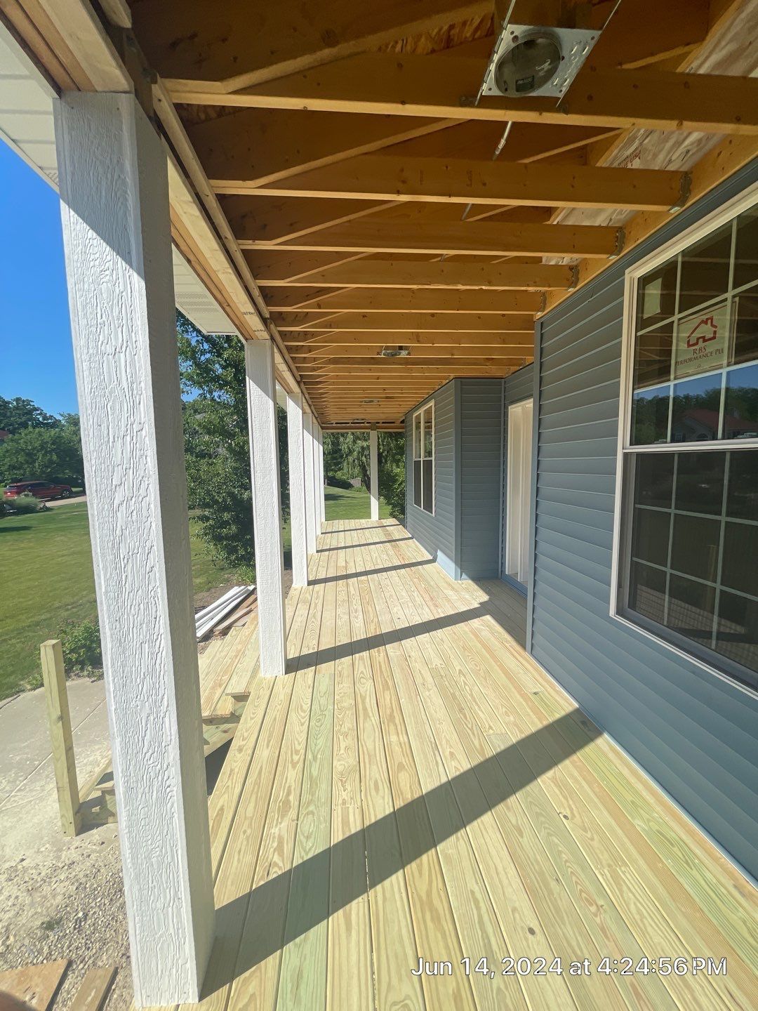 A long wooden porch with a fan on the ceiling of a house.