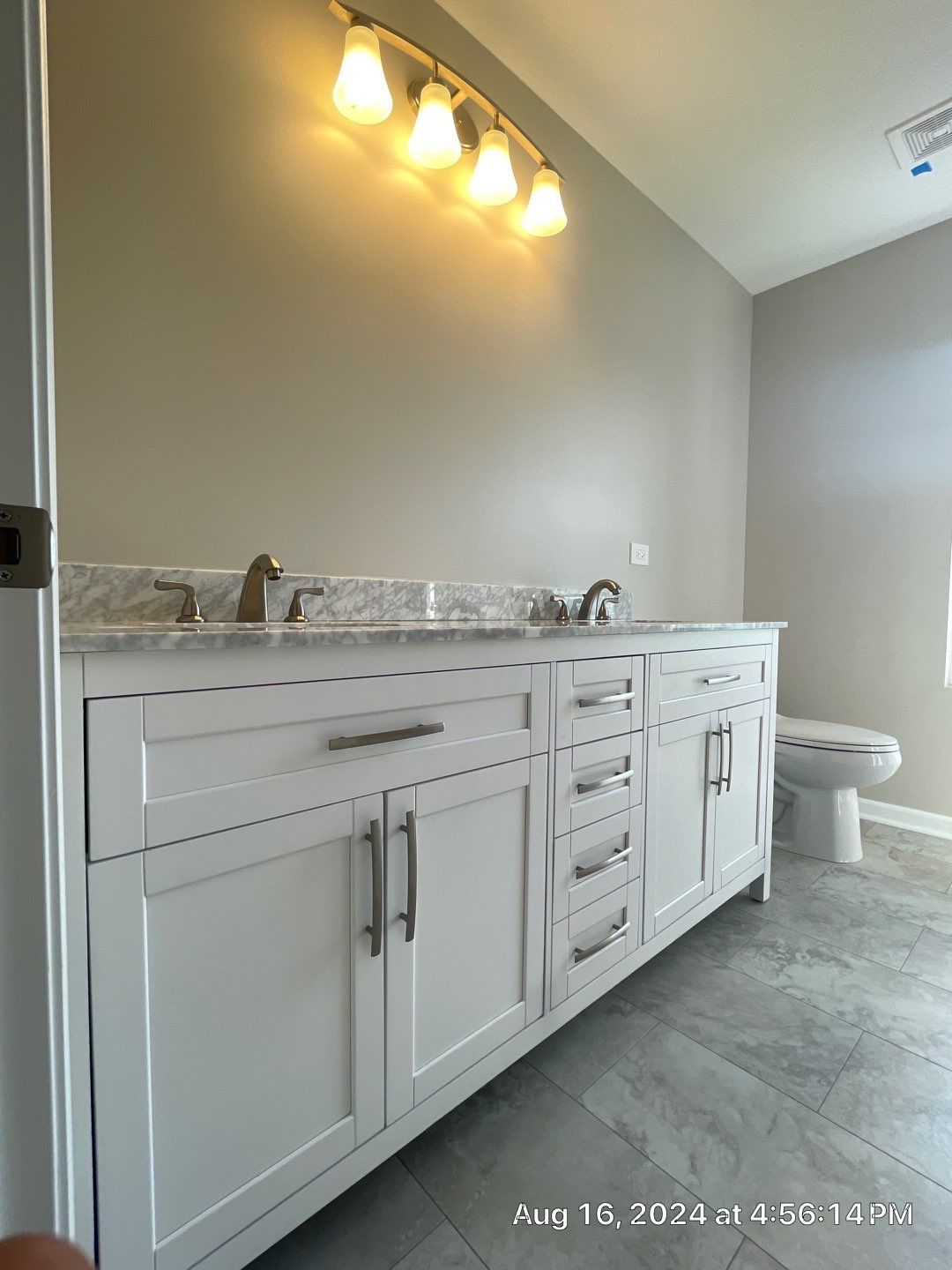 A bathroom with two sinks , a toilet , and a light fixture.