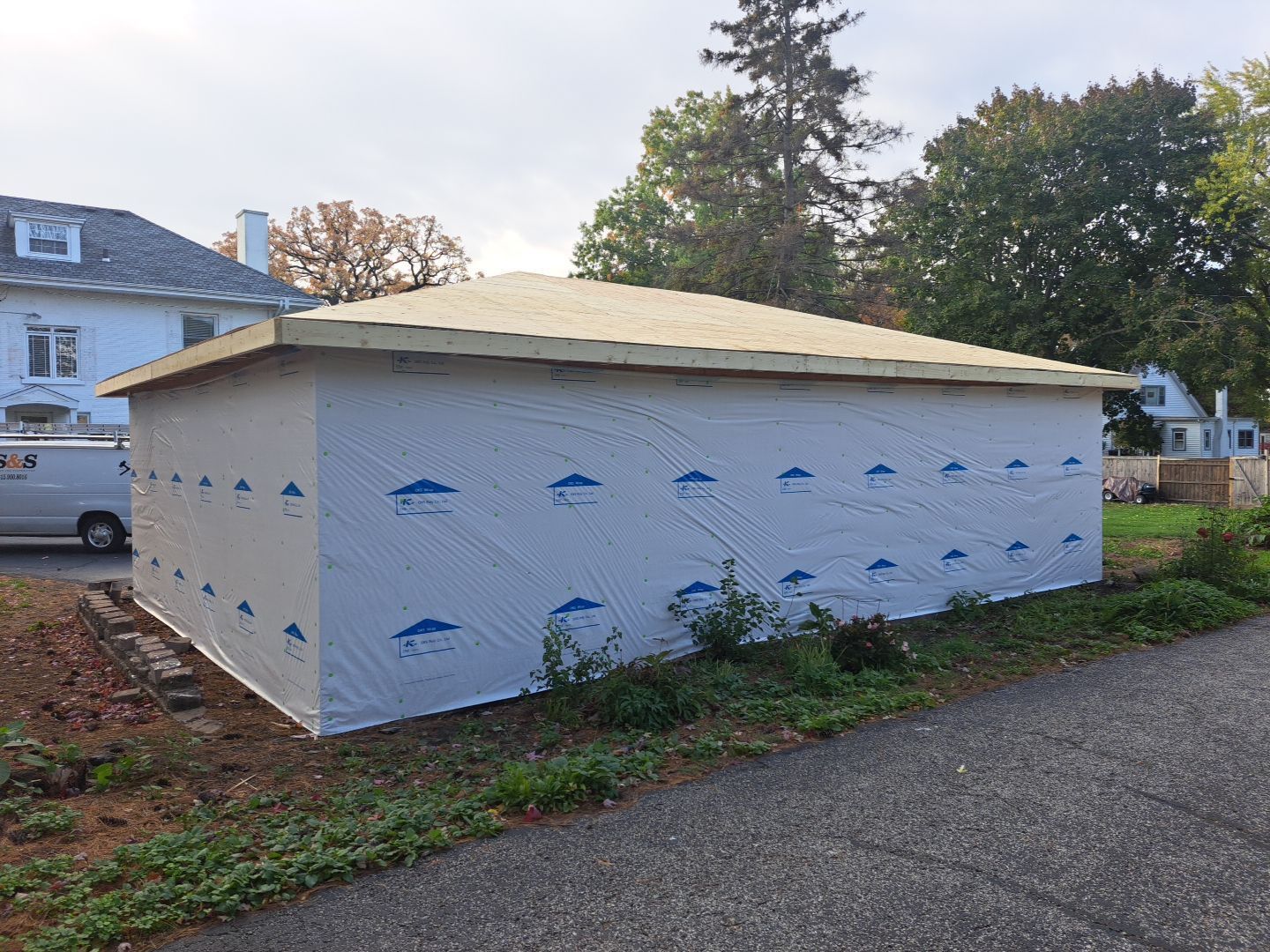 A garage is being built on the side of a road next to a house.