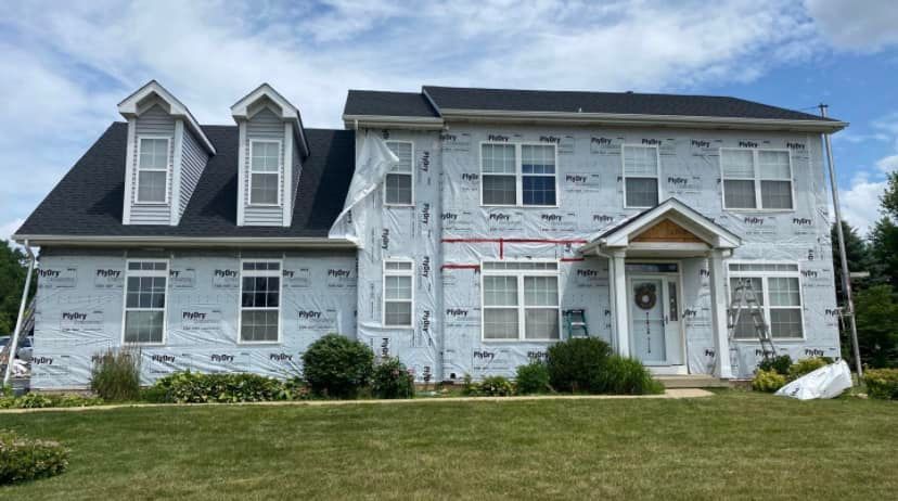 A large white house with a black roof is being remodeled.