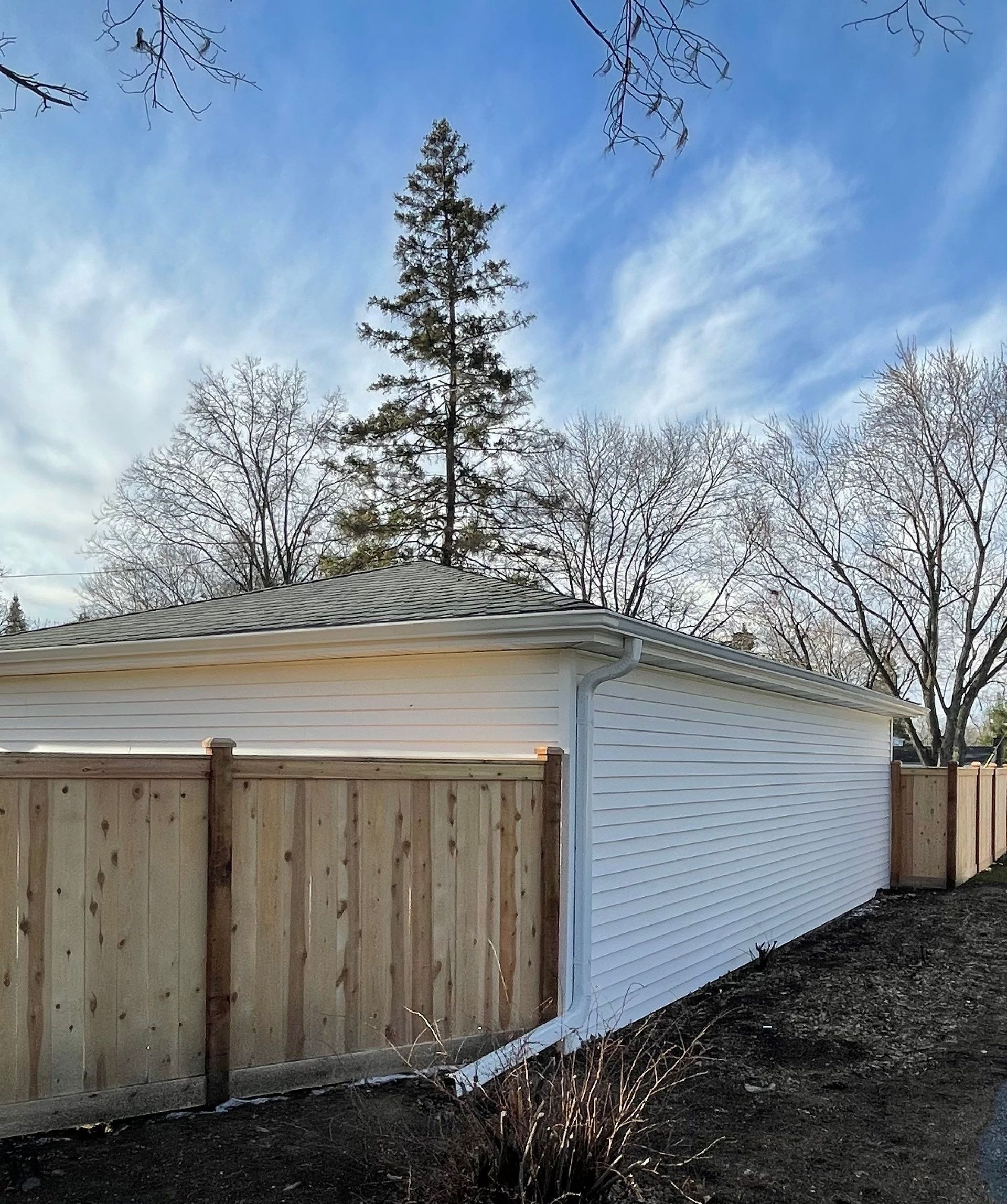 A white garage with a wooden fence and trees in the background.