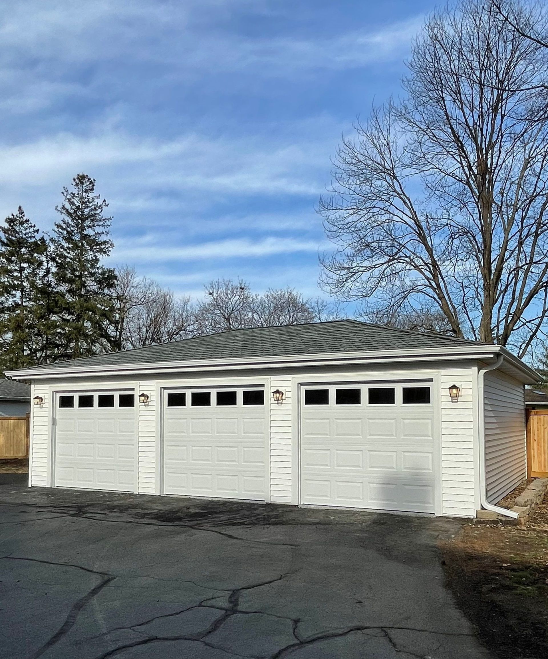 A white garage with three garage doors is in the driveway of a house.
